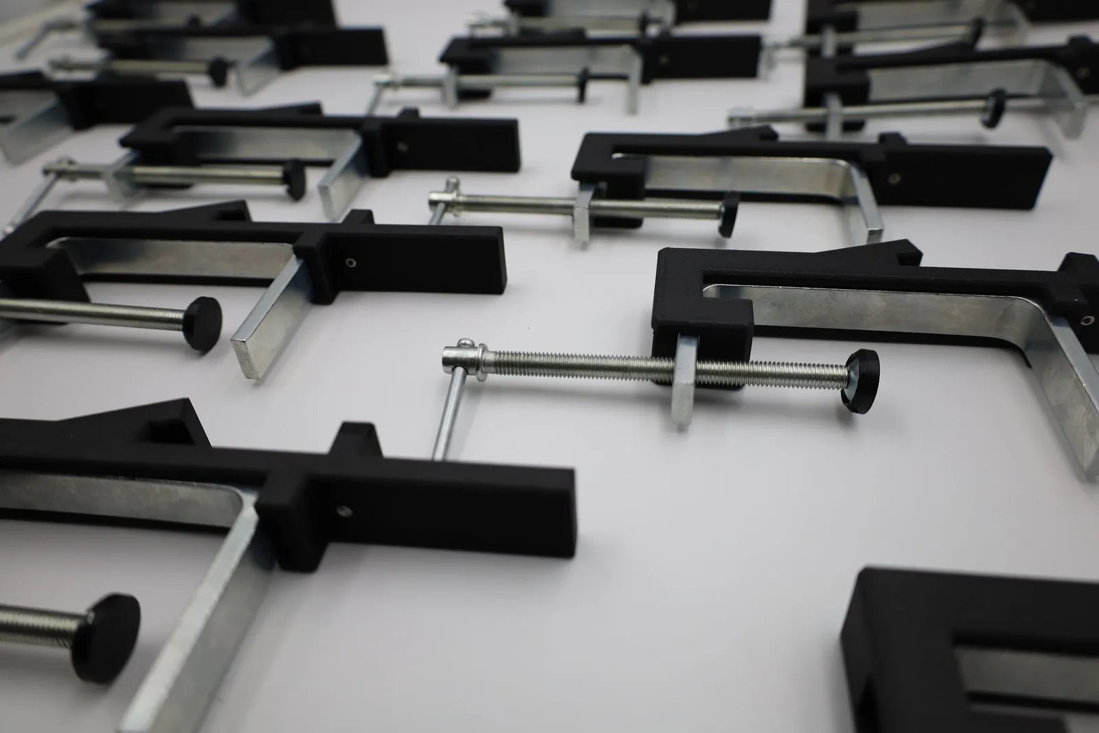 Close view of assembled clamps: matte black printed arms on galvanised steel frames, each screw ending in a black pad