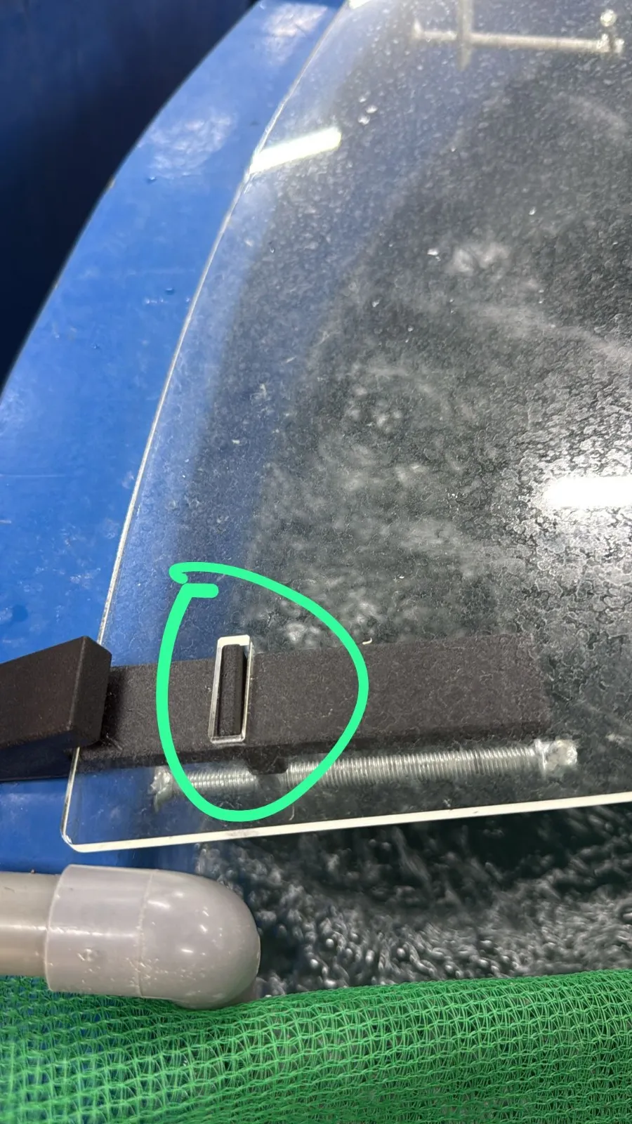 The prototype clamp on a blue tank's rim with a clear acrylic panel on its arm, the arm's tab through a slot in the panel ringed in green marker