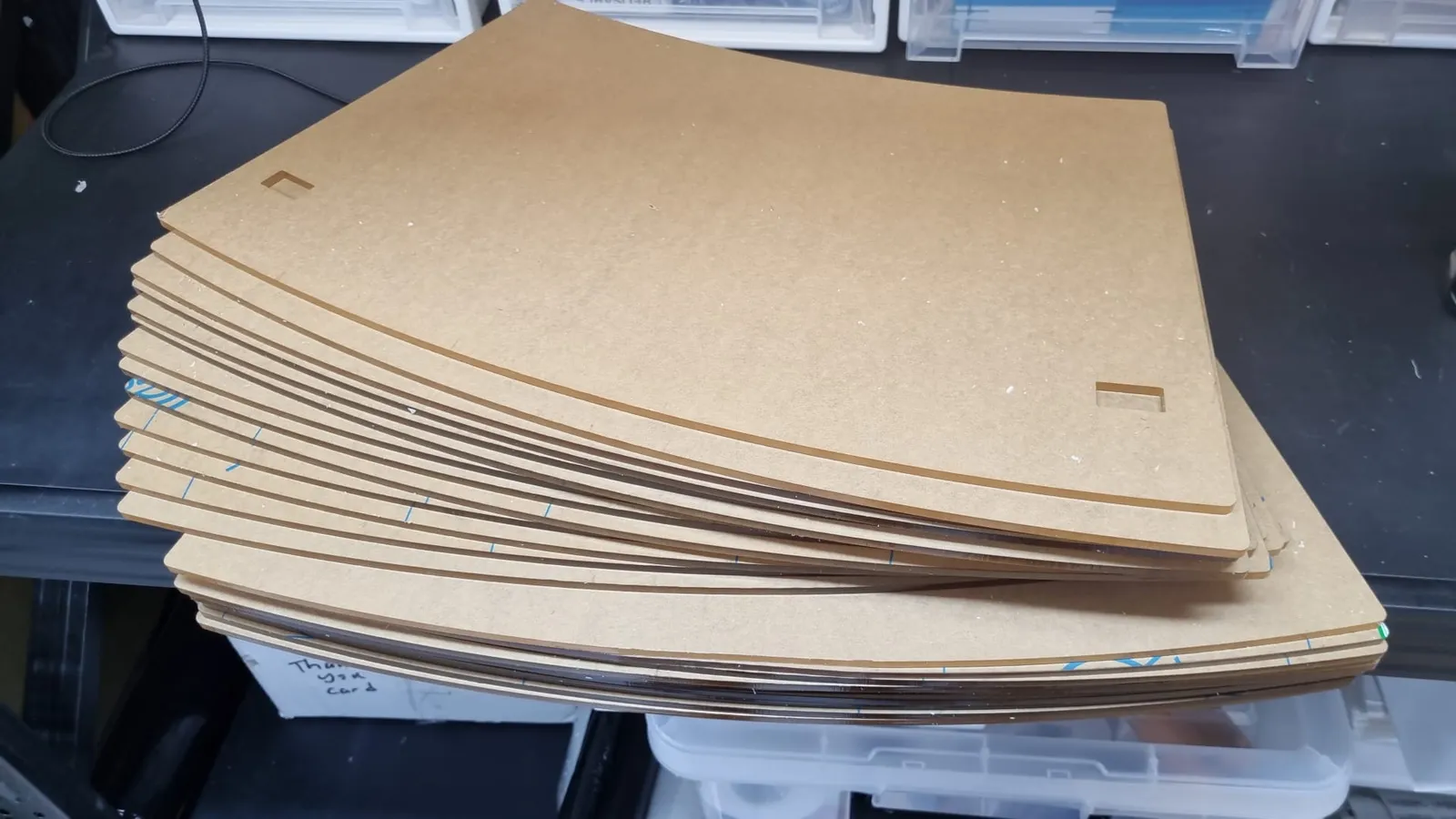 A stack of curved acrylic segments still in their brown protective film, each with two rectangular slots for the clamp tabs