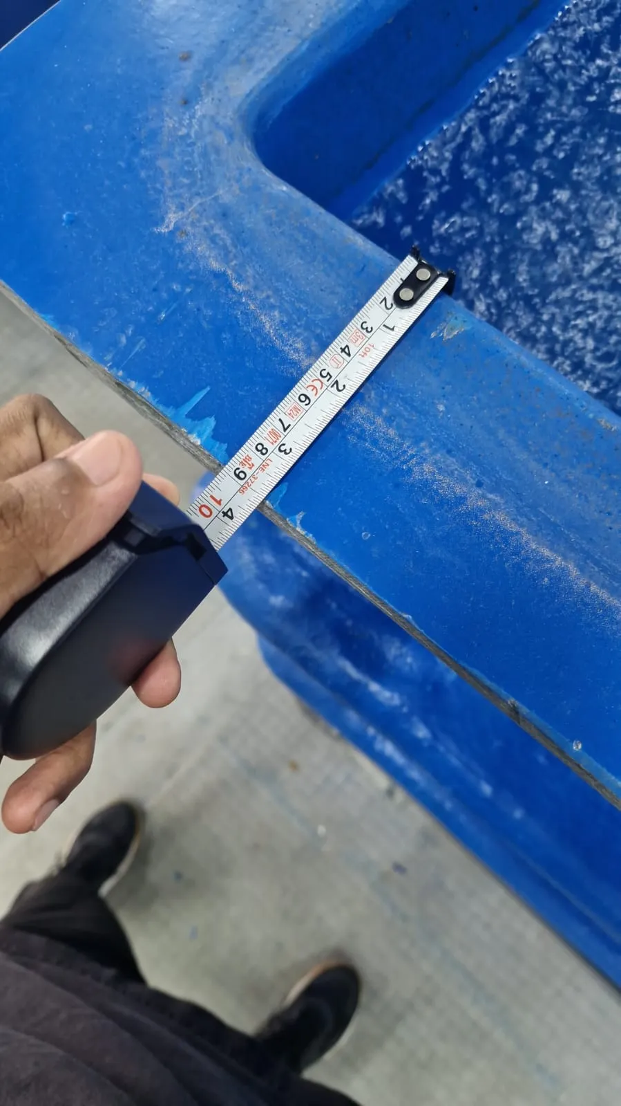 A tape measure across the top of a blue fish tank's rim at the farm, measuring its width