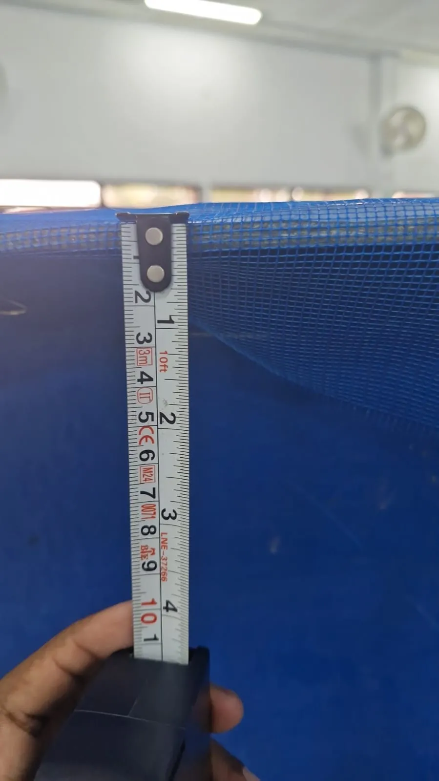A tape measure held down the inside wall of a blue fish tank under a net, measuring the rim's depth