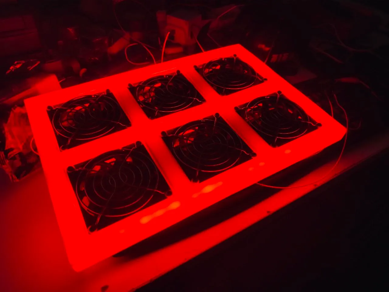 The same six-fan panel switched on in a dark room, its white frame glowing bright red around the fans