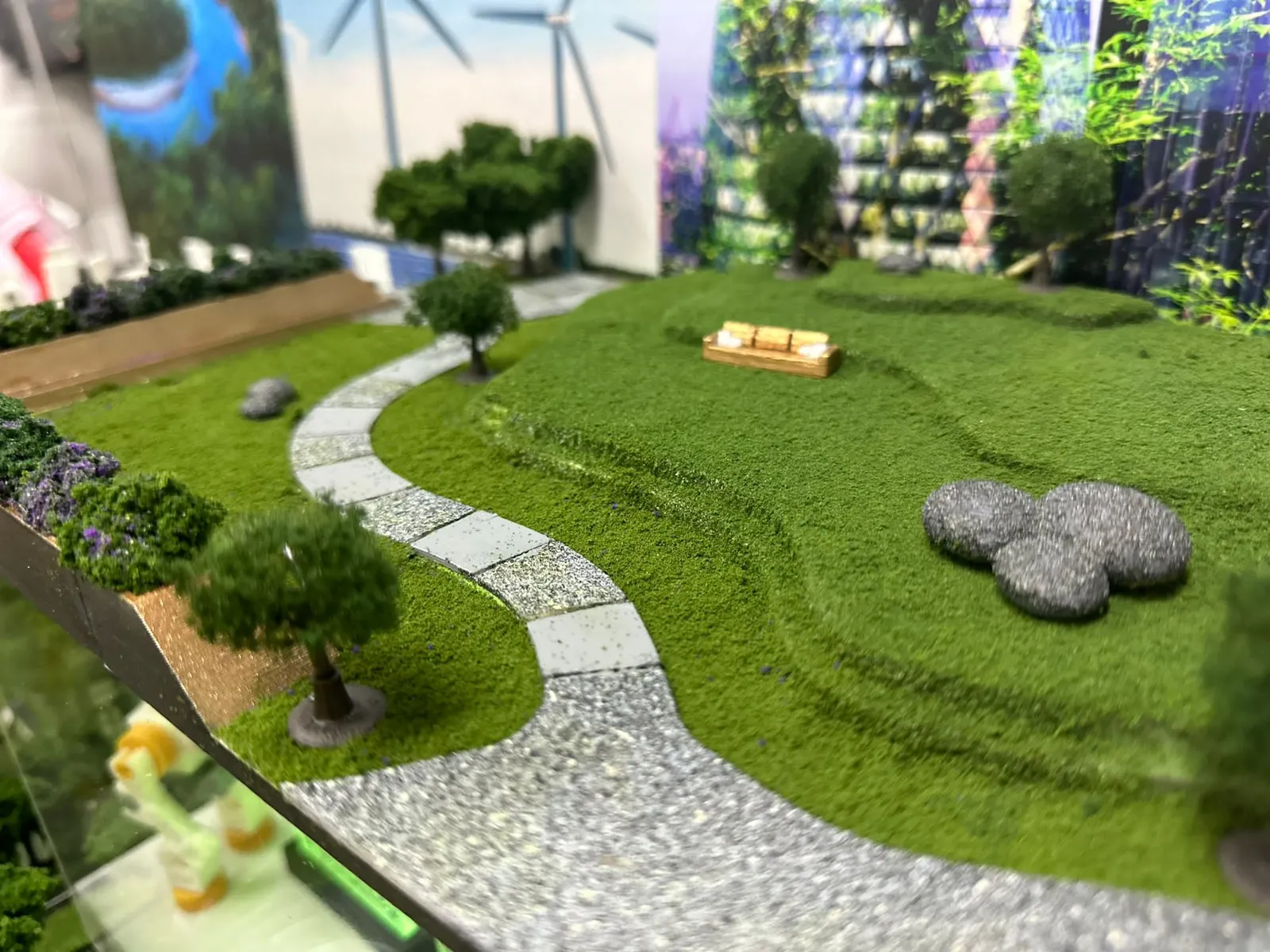 The park on the roof of the future data centre: rolling grass, a curving stone path, model trees, grey boulders and a small bench