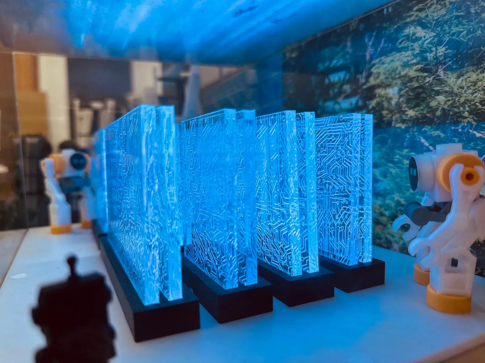Close-up of the clear panels patterned with circuit lines, glowing blue on black stands, with small robot figures either side