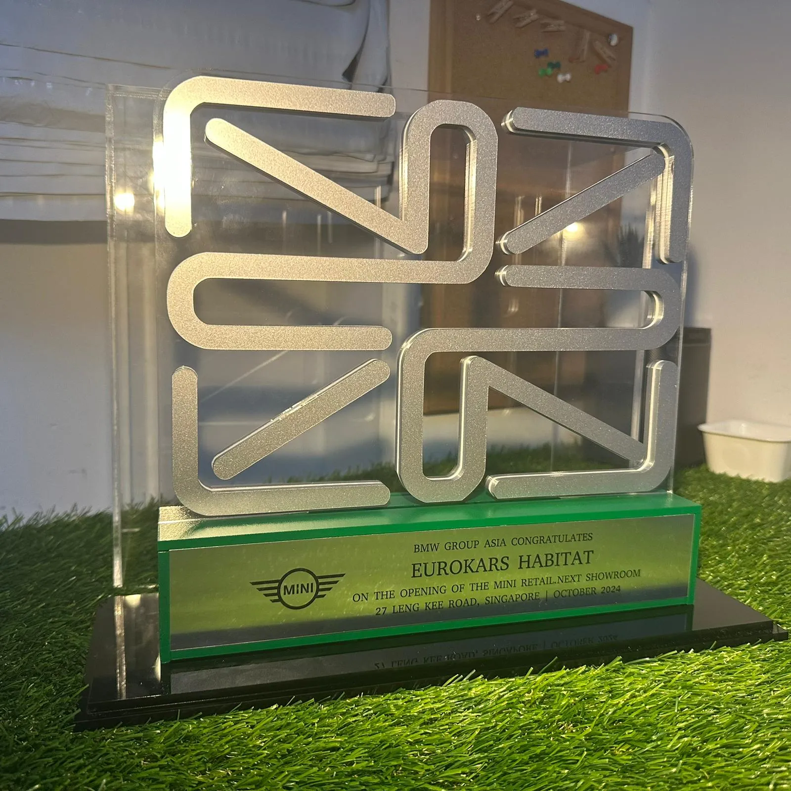 The finished MINI award without its cover, seen at an angle: the silver Union Jack on clear acrylic above the green base and engraved plate