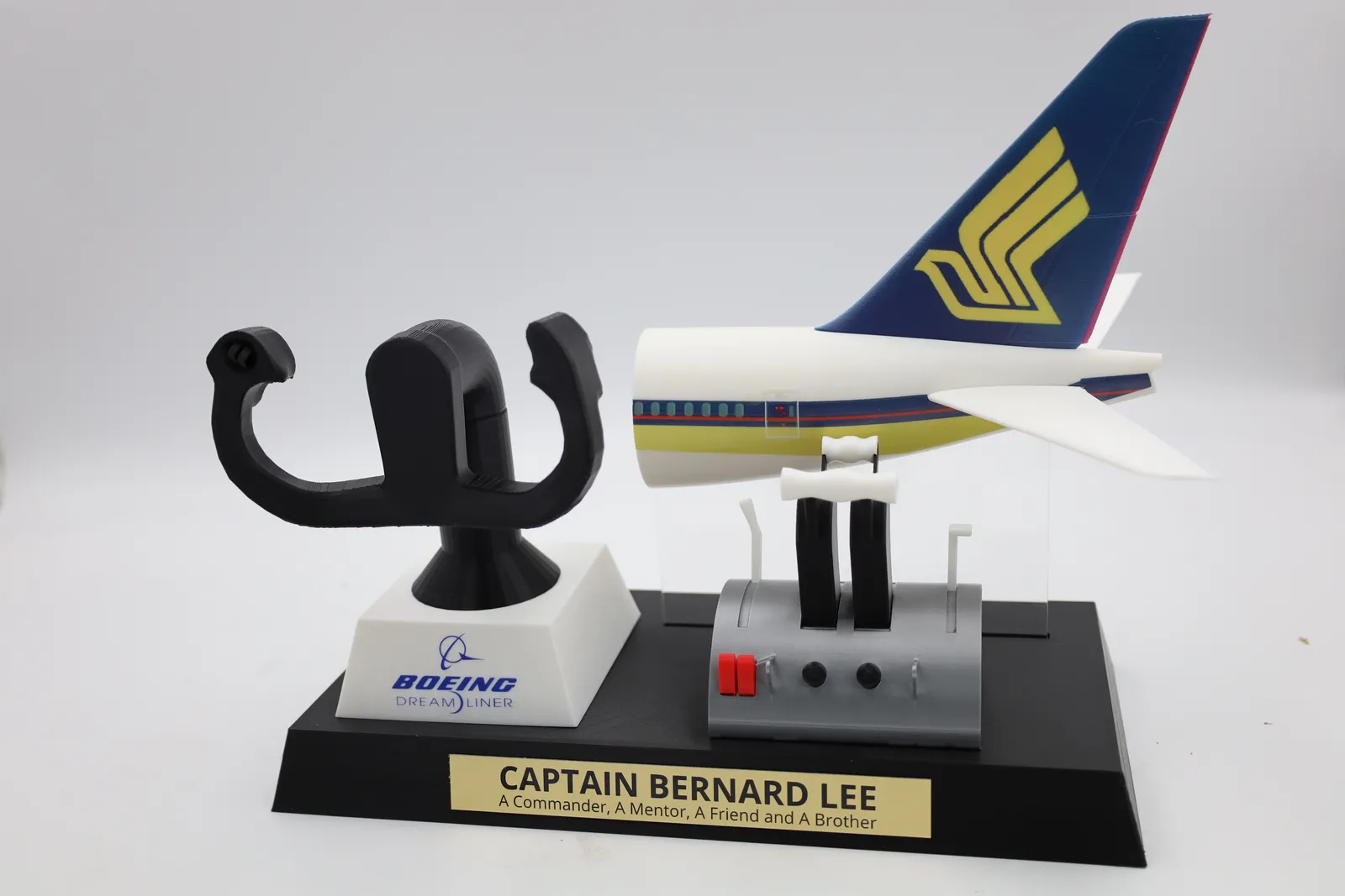 The finished captain trophy: a black control yoke on a white Boeing Dreamliner pedestal, a grey throttle column and a Boeing 787 tail in Singapore Airlines colours on a black base with a gold nameplate for Captain Bernard Lee