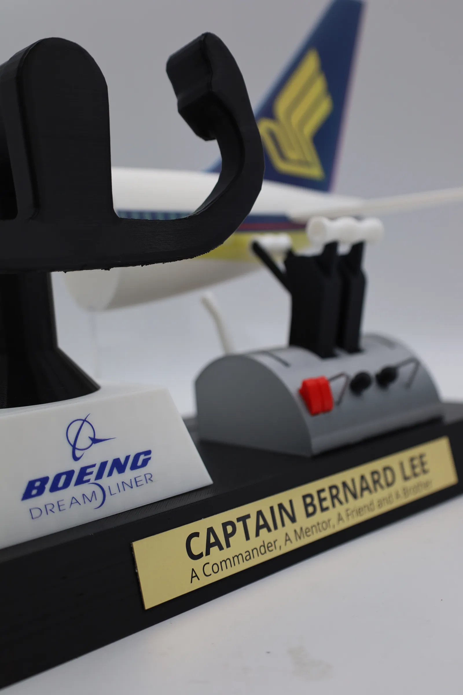 Close up of the trophy base: the Boeing Dreamliner logo on the white yoke pedestal, the grey throttle with red switches, and the gold nameplate reading Captain Bernard Lee, A Commander, A Mentor, A Friend and A Brother