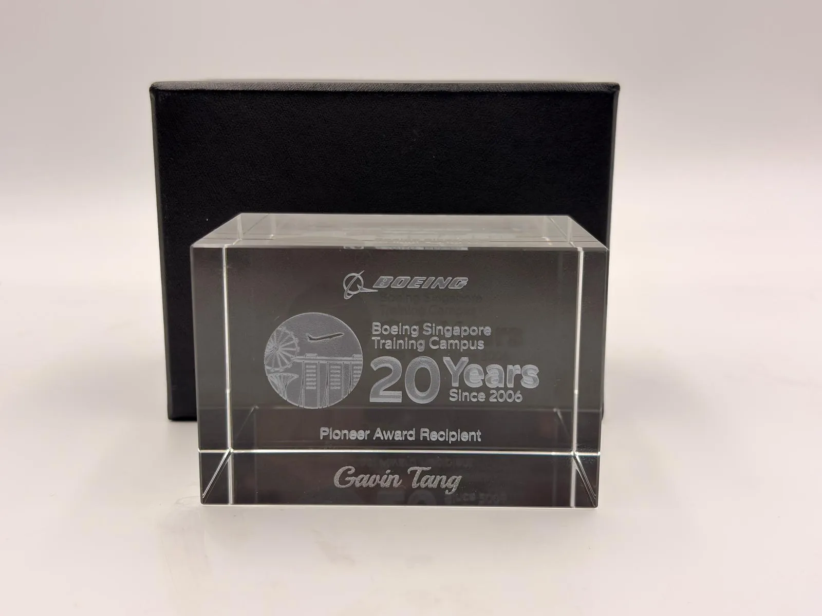 A clear crystal block engraved with the Boeing Singapore Training Campus 20 Years artwork and the name Gavin Tang, in front of a black box