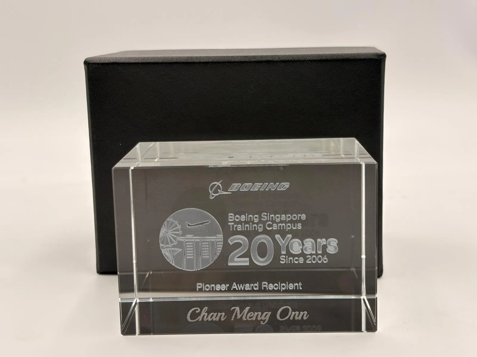 A clear crystal block engraved with the name Chan Meng Onn, in front of a black box