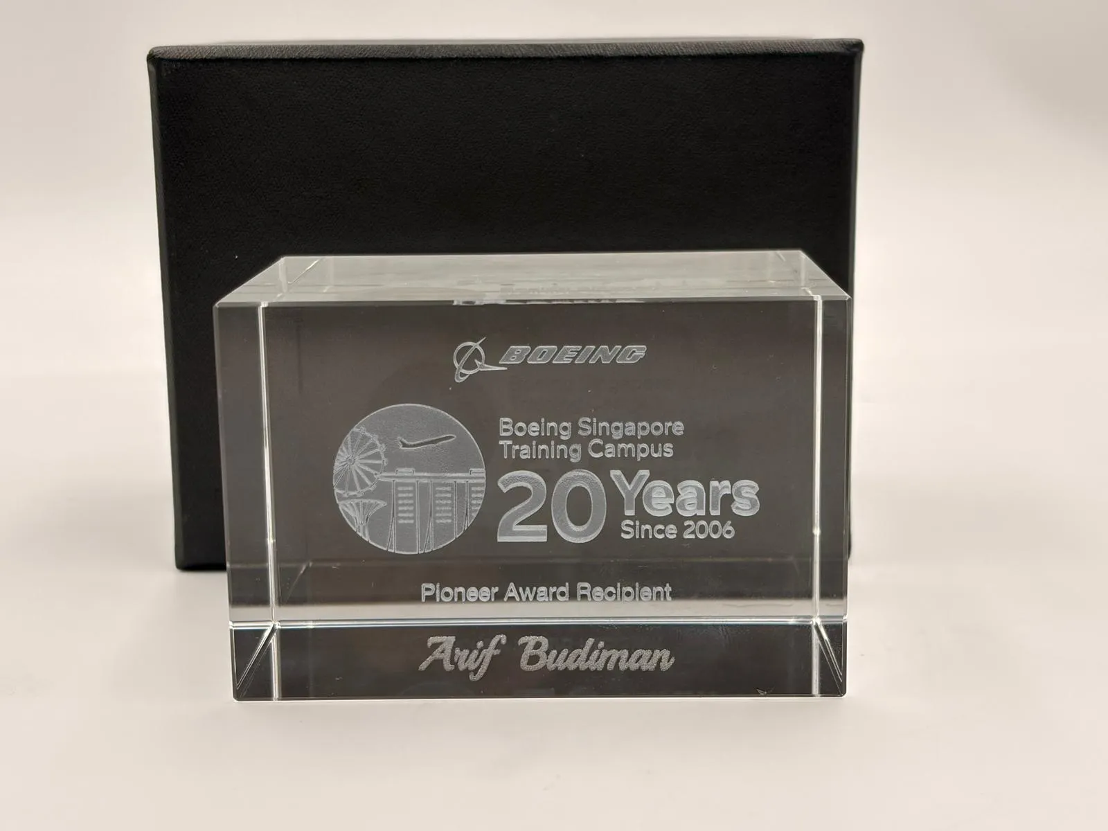 A clear crystal block engraved with the name Arif Budiman, in front of a black box