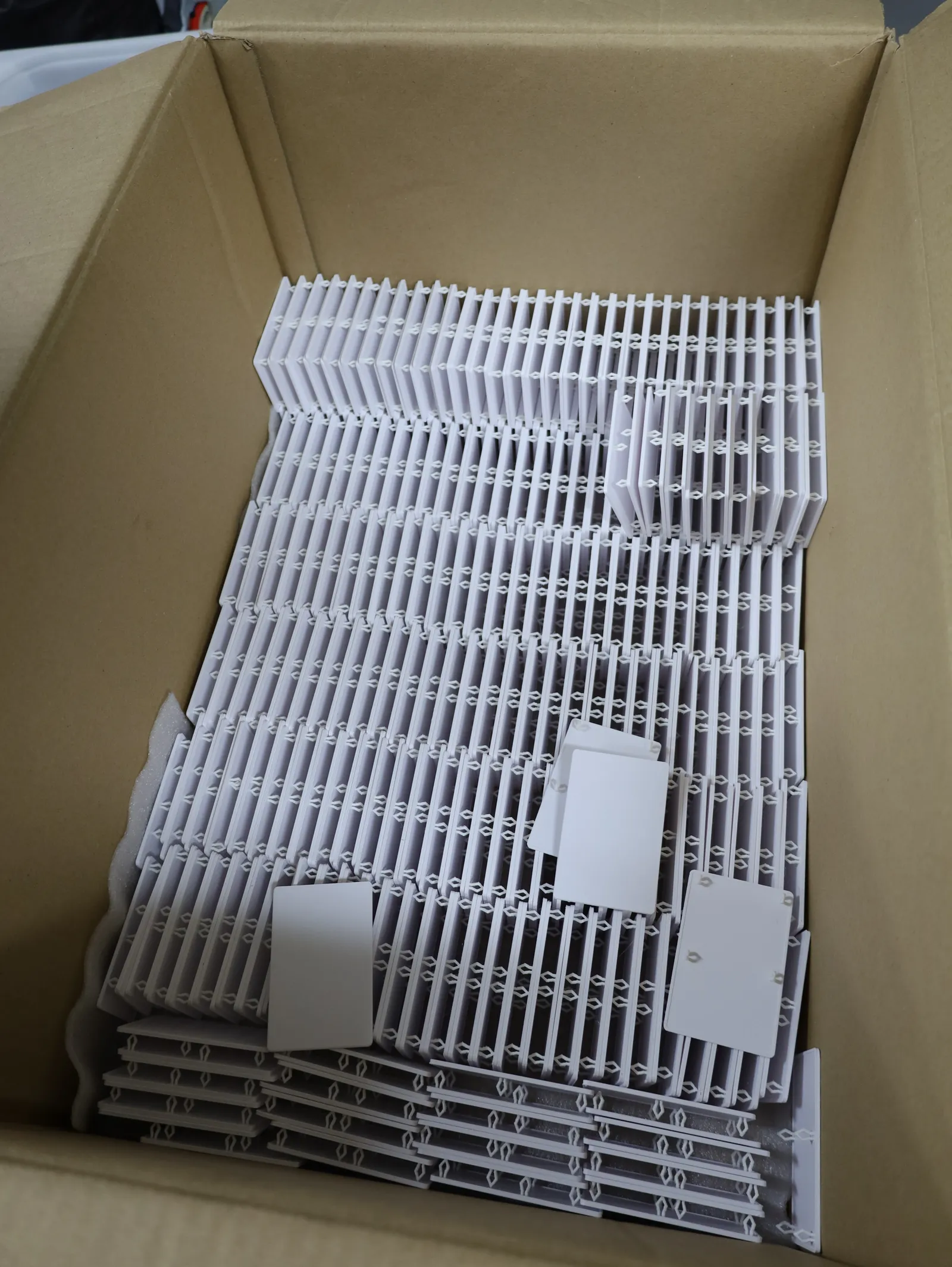 Looking down into an open carton of white fridge covers packed on edge in rows, with a few loose covers lying flat on top