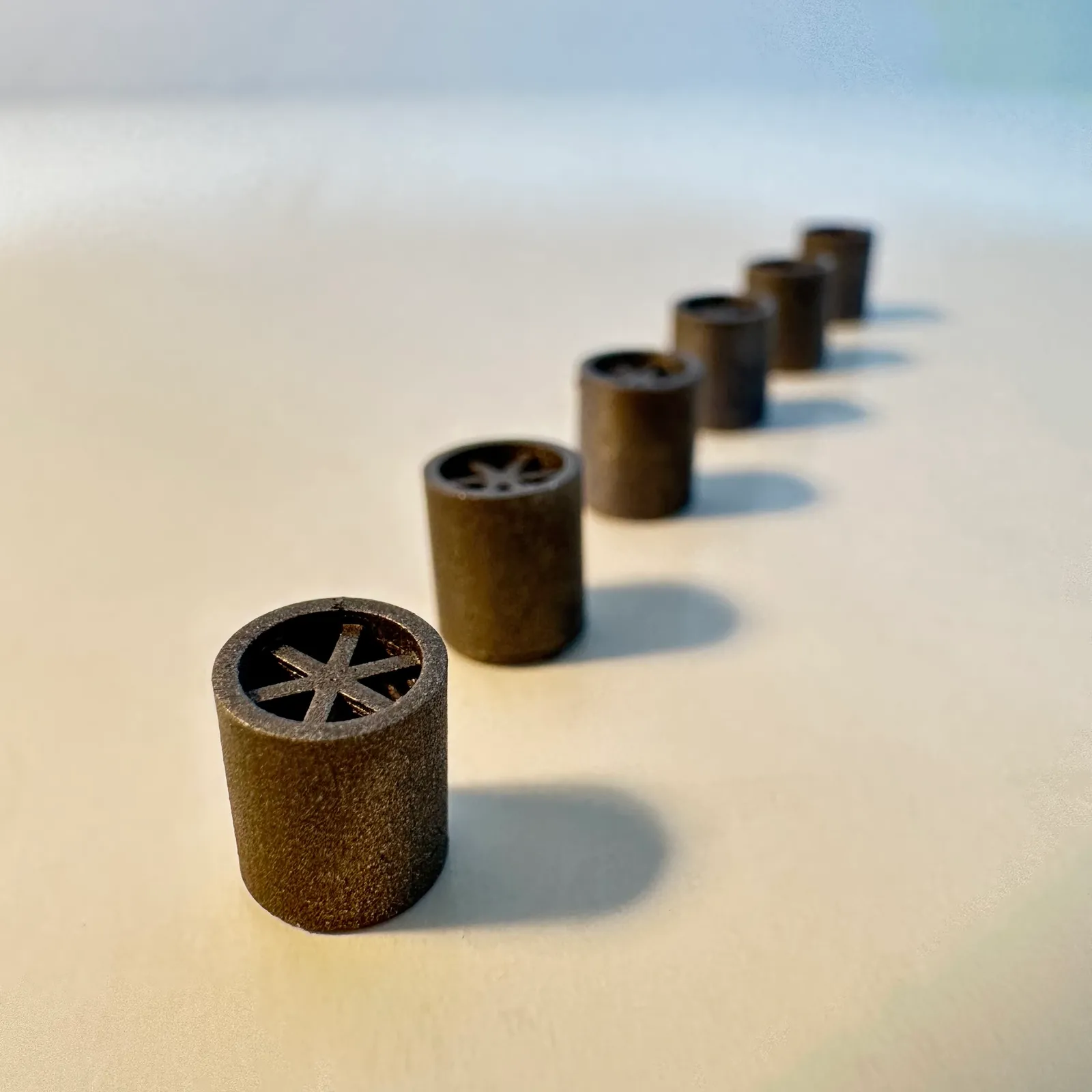 A row of black printed spares standing in a line on a white table, the nearest one showing its six-spoke end