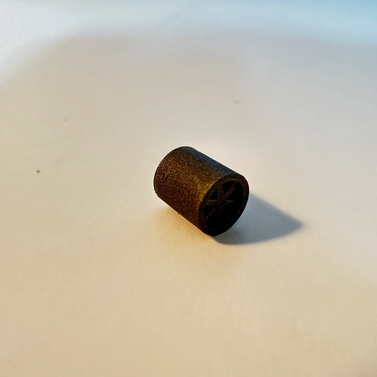 One black spare lying on its side on a white table, its spoked end facing the camera and the matt surface of its wall in the light
