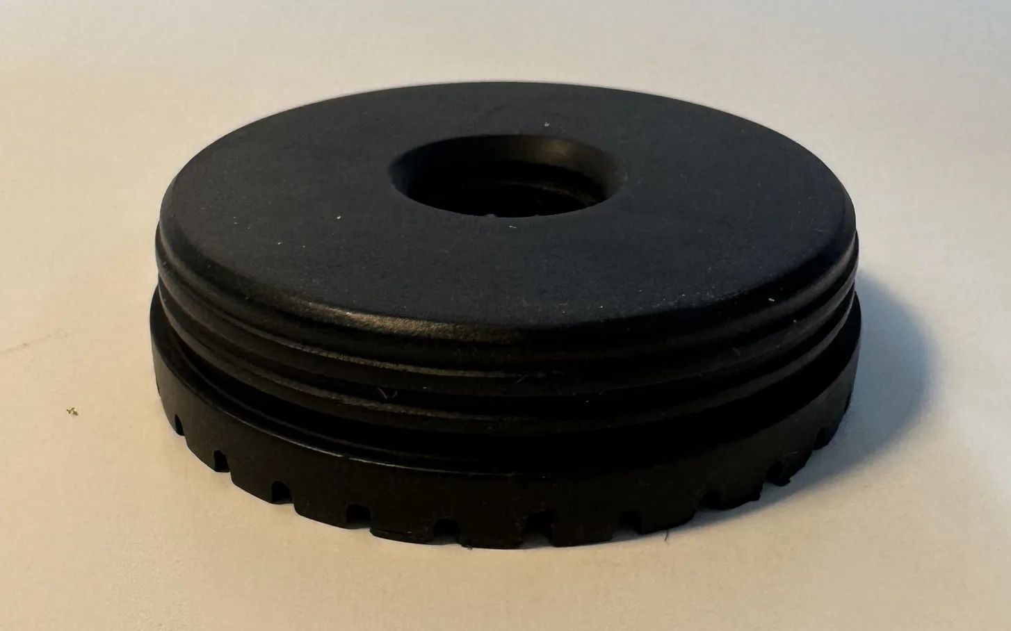 The finished black rubber grommet at an angle, showing its smooth top face, the central bore, the ribs around the side and the teeth below