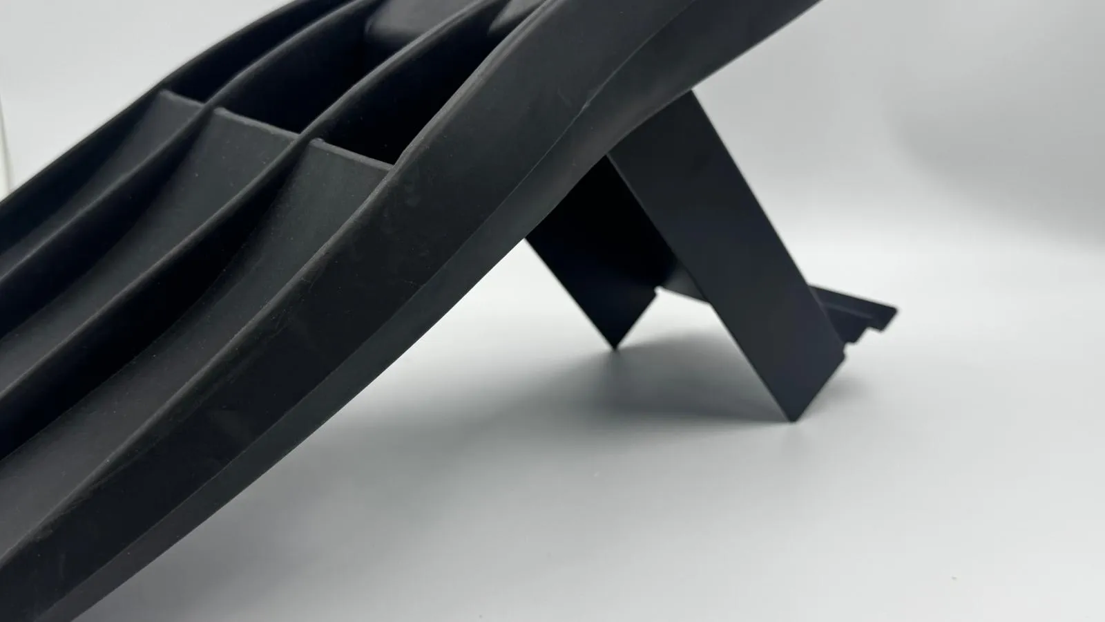 A black dive fin resting on the matt black fin stand, seen low from the side