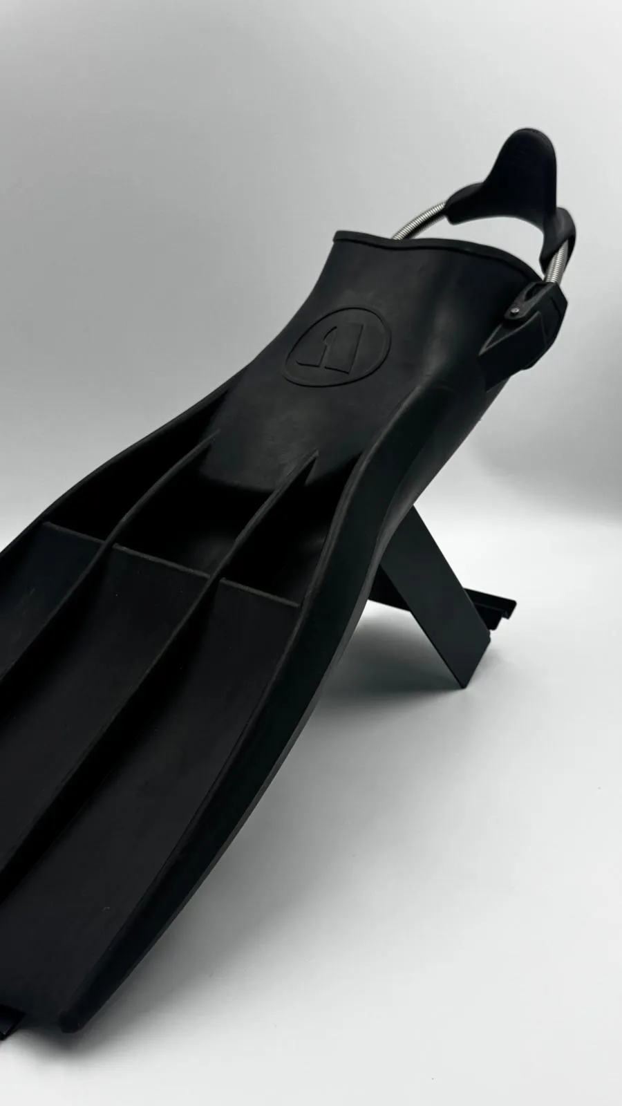 A black dive fin with a spring strap angled up on the matt black fin stand