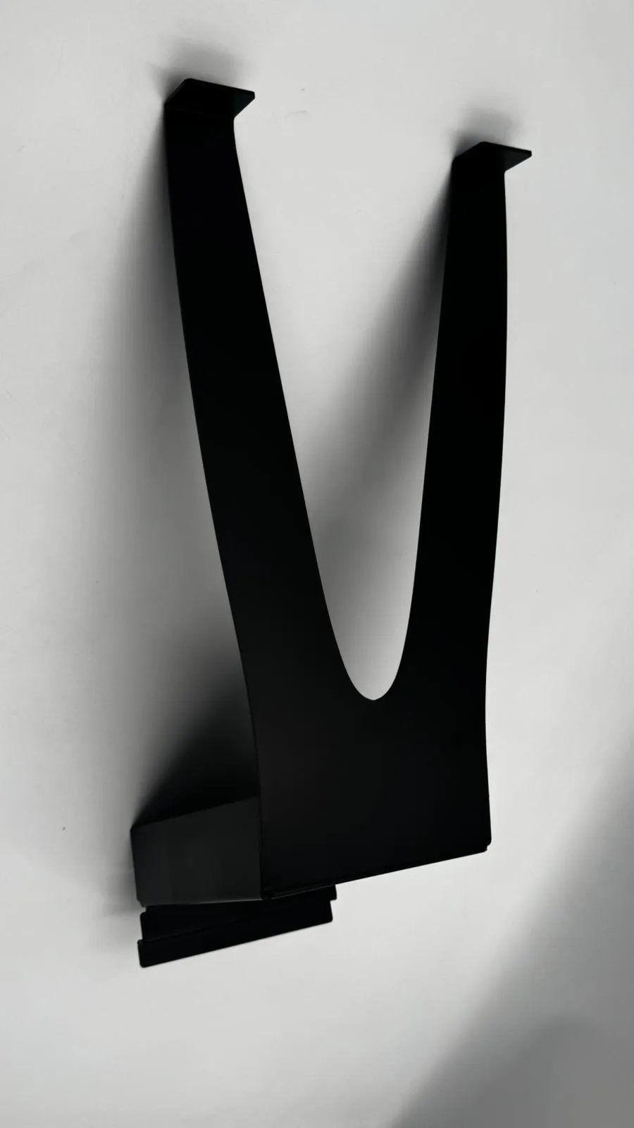 The matt black fin stand seen from the front, its two legs meeting in a V below the slatwall hook