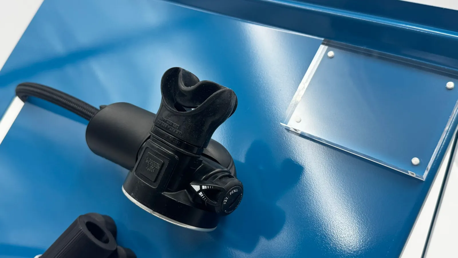 Close-up of a regulator mouthpiece on the blue panel beside the clear acrylic plate on its four standoffs