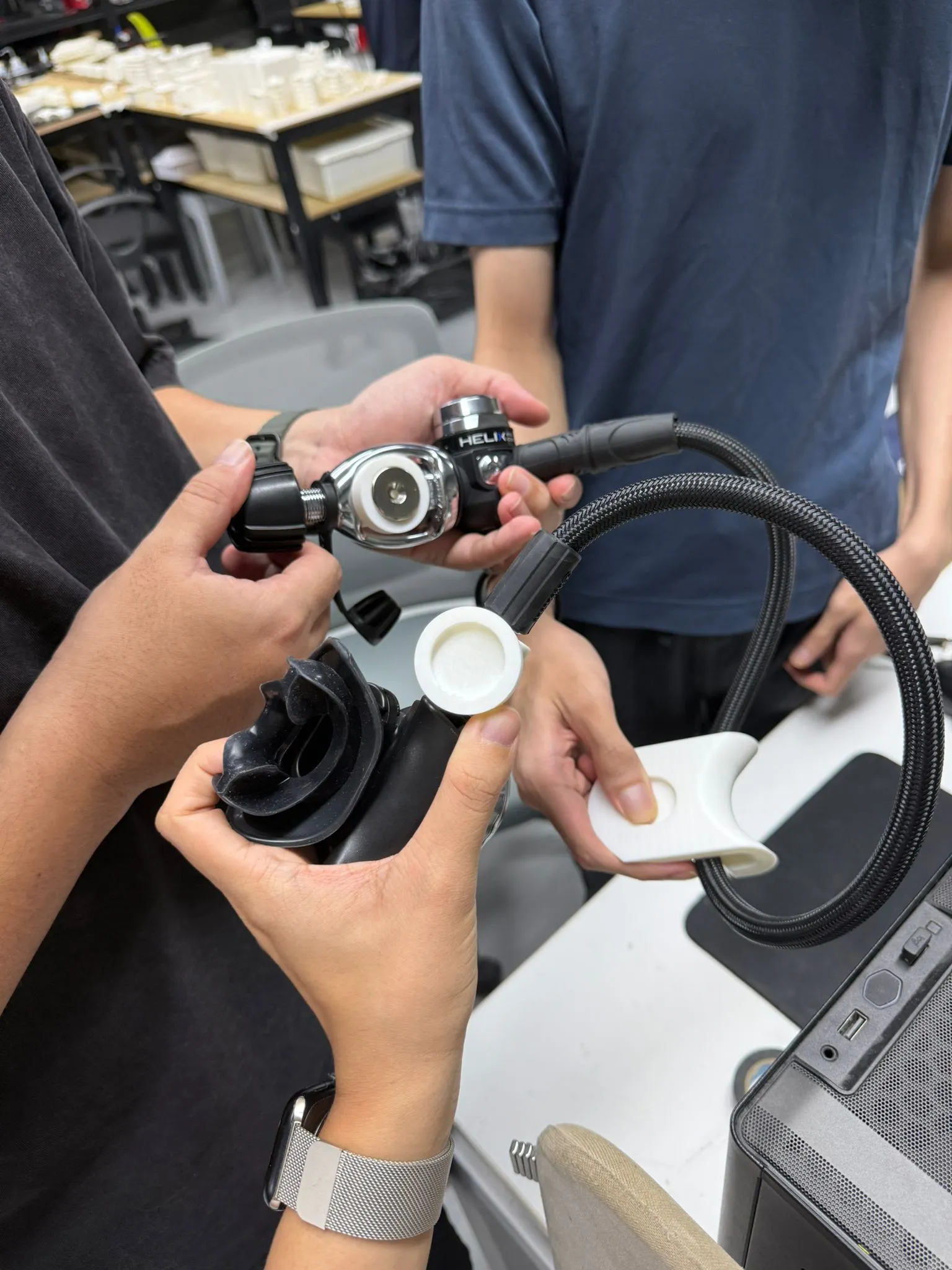 Hands holding a regulator, its hose and a white printed test holder beside the mouthpiece