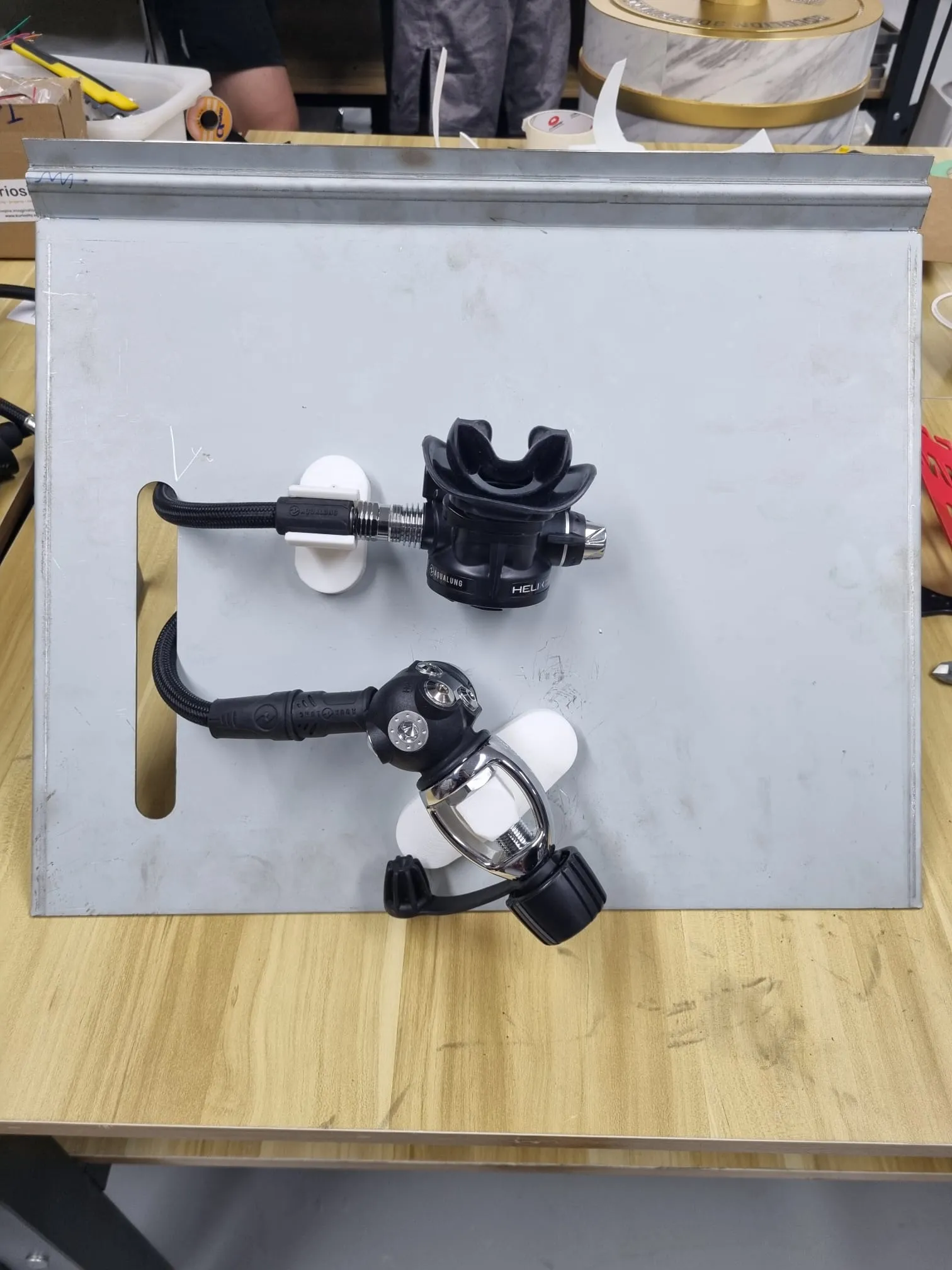The unpainted steel prototype panel on a workbench, a regulator held on white printed holders with its hose running through the slot