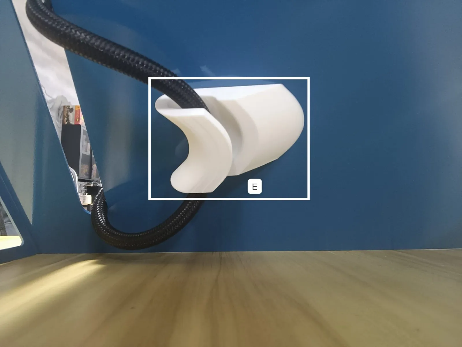 Close-up of white holder E cradling a regulator hose on a blue panel, boxed and labelled