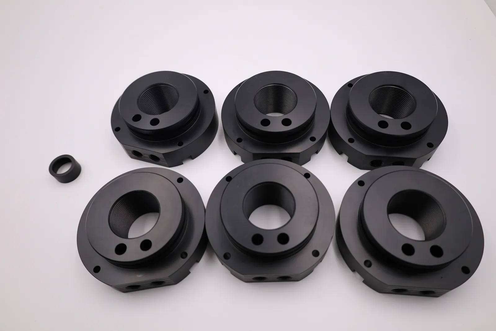 Six black POM-C fuel filling lids, CNC machined, laid out in two rows on a white table, each with a threaded centre bore and four bolt holes