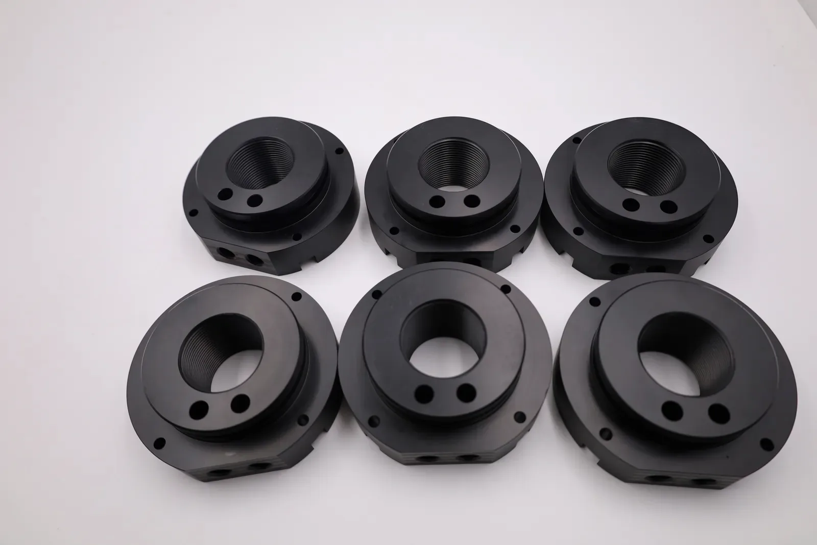 Six black POM-C fuel filling lids, CNC machined, laid out in two rows on a white table, each with a threaded centre bore and bolt holes