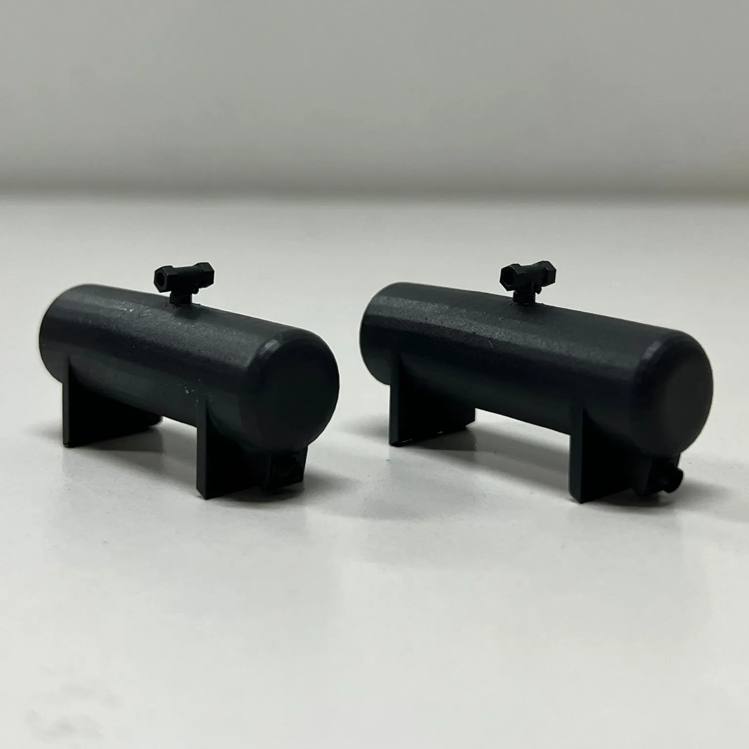 Two small printed tanks in dark grey, each a separate part, standing side by side on a white table