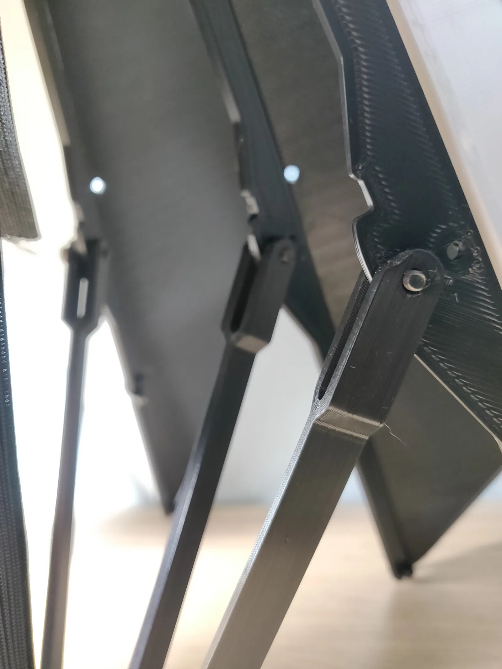 Close-up of a black 3D printed arm pinned to the edge of a panel, with more arms and hinges behind it