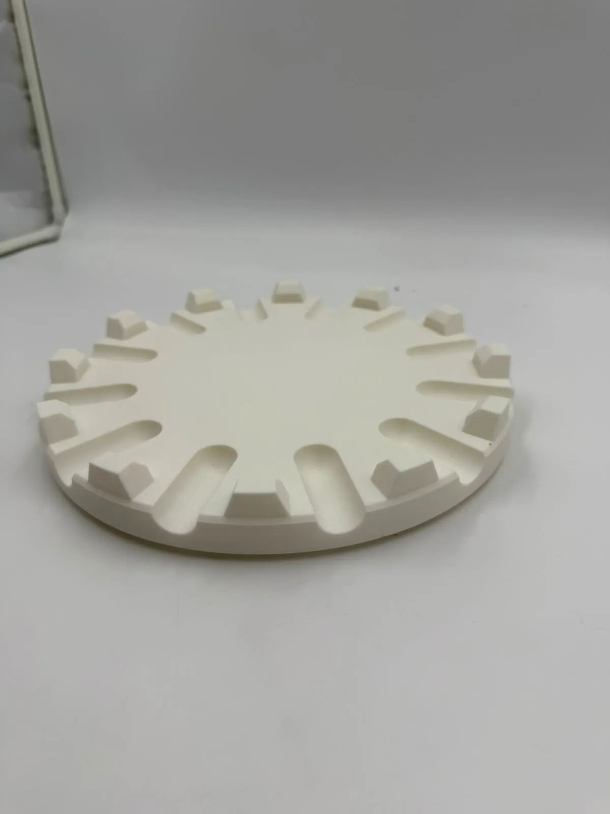 The white 3D printed cake plate holder: a round base with 12 rounded lift slots and 12 raised blocks around the edge