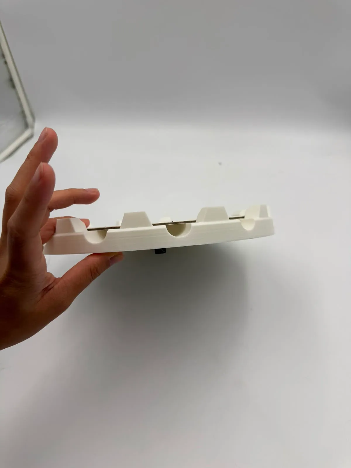 The holder held side-on in a hand, showing the raised blocks and the rounded lift slots cut into the rim