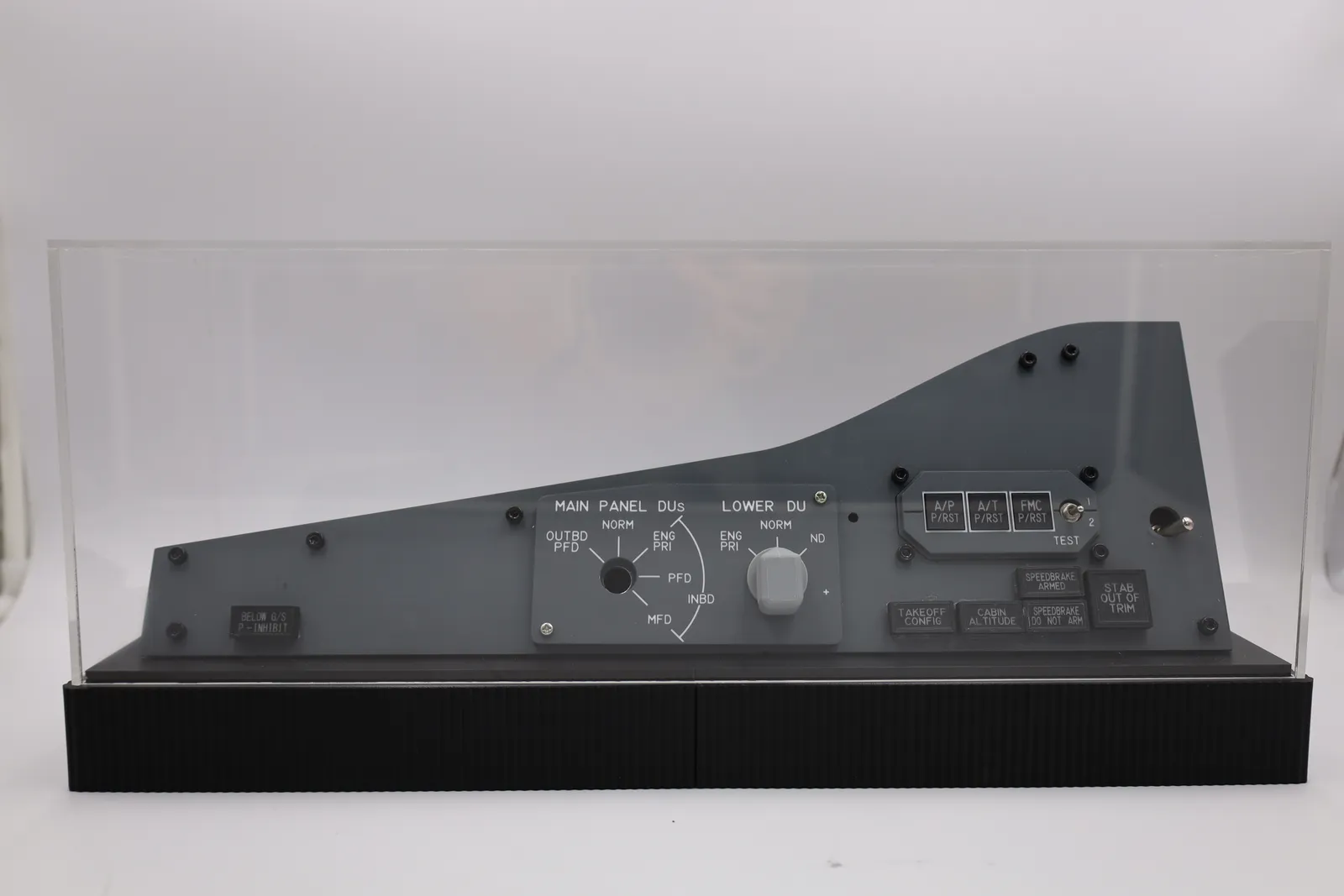 The finished enclosure from the front: a grey cockpit-style control panel standing on a ribbed matte black base under a clear acrylic cover