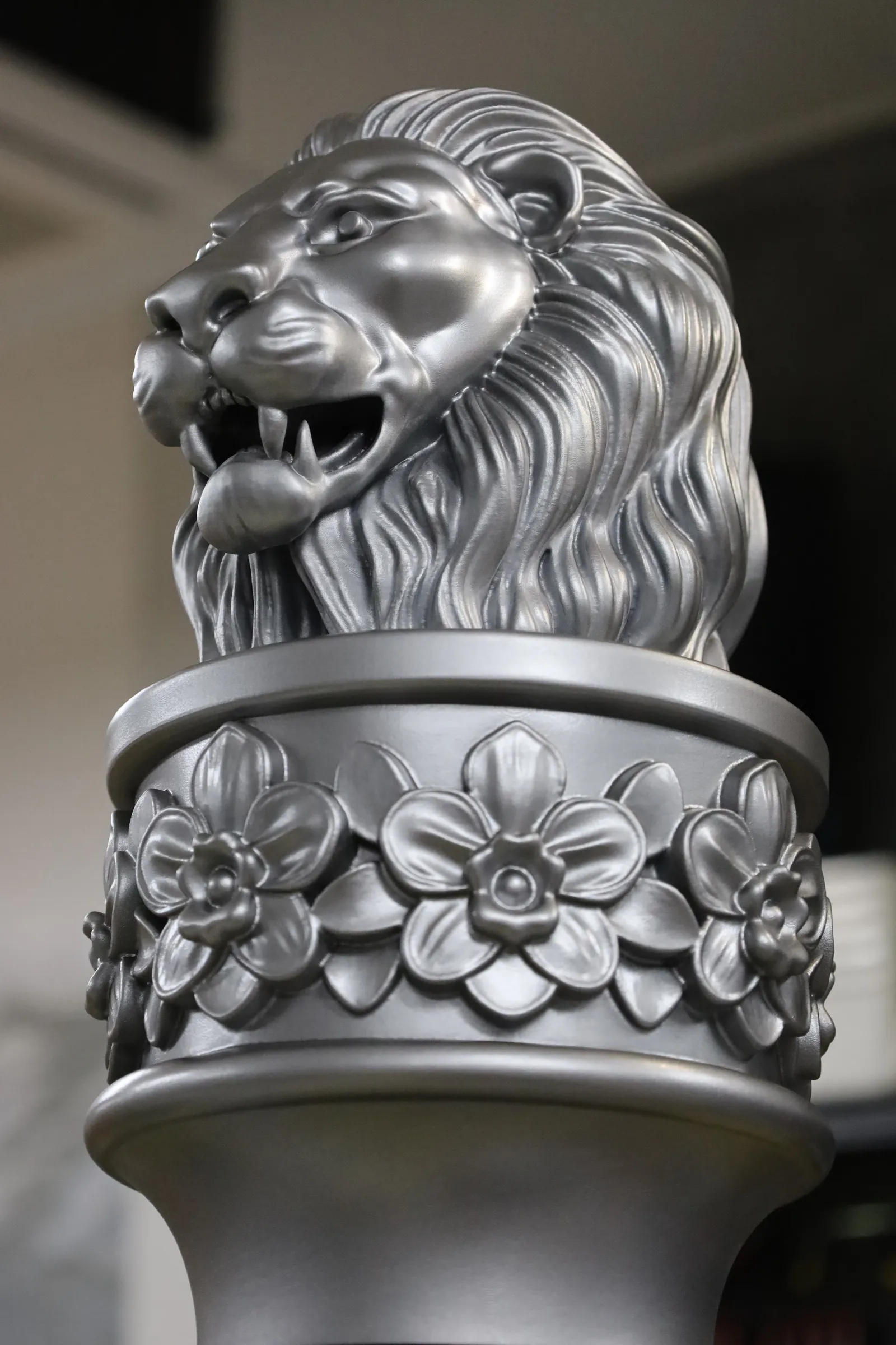 The silver lion head of the Curtin Singapore mace, mouth open, sitting on a collar of raised orchids