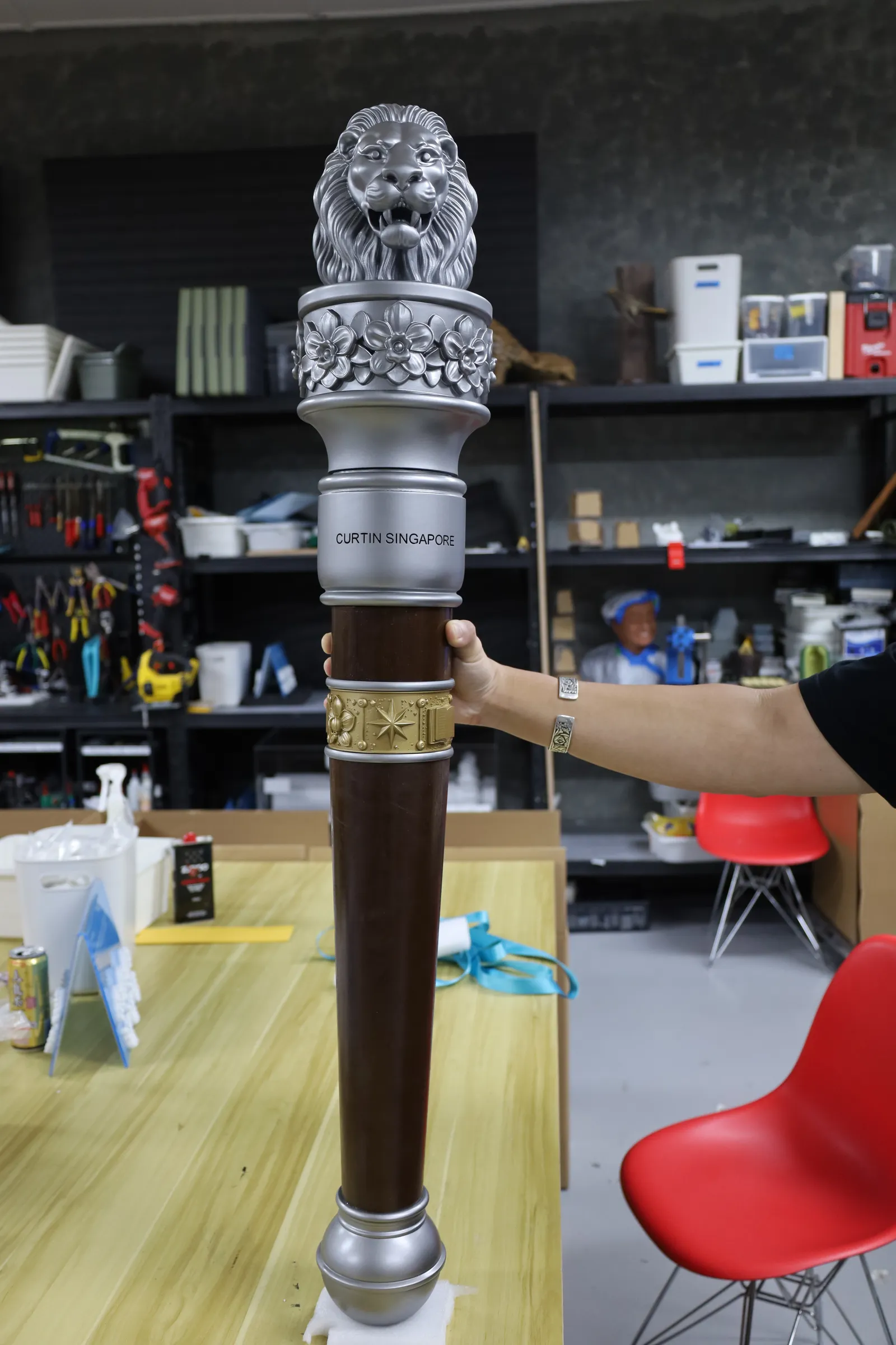 The whole finished Curtin Singapore mace held upright, from the silver lion head and orchid collar down the brown shaft to the silver pommel