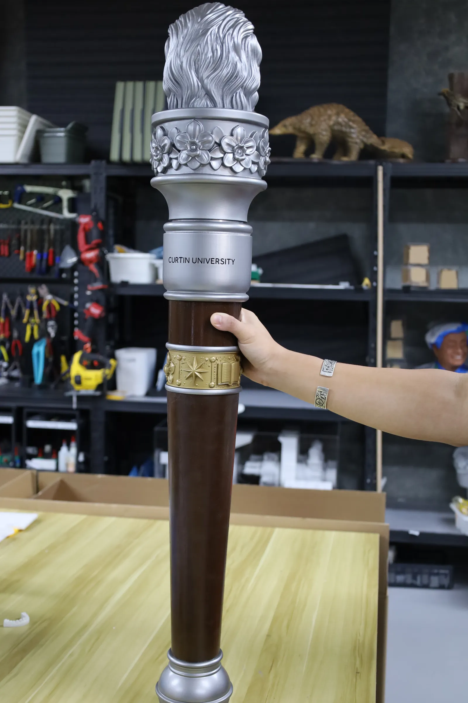 The back of the finished mace held upright, with CURTIN UNIVERSITY on the ring and the gold heritage band on the brown shaft