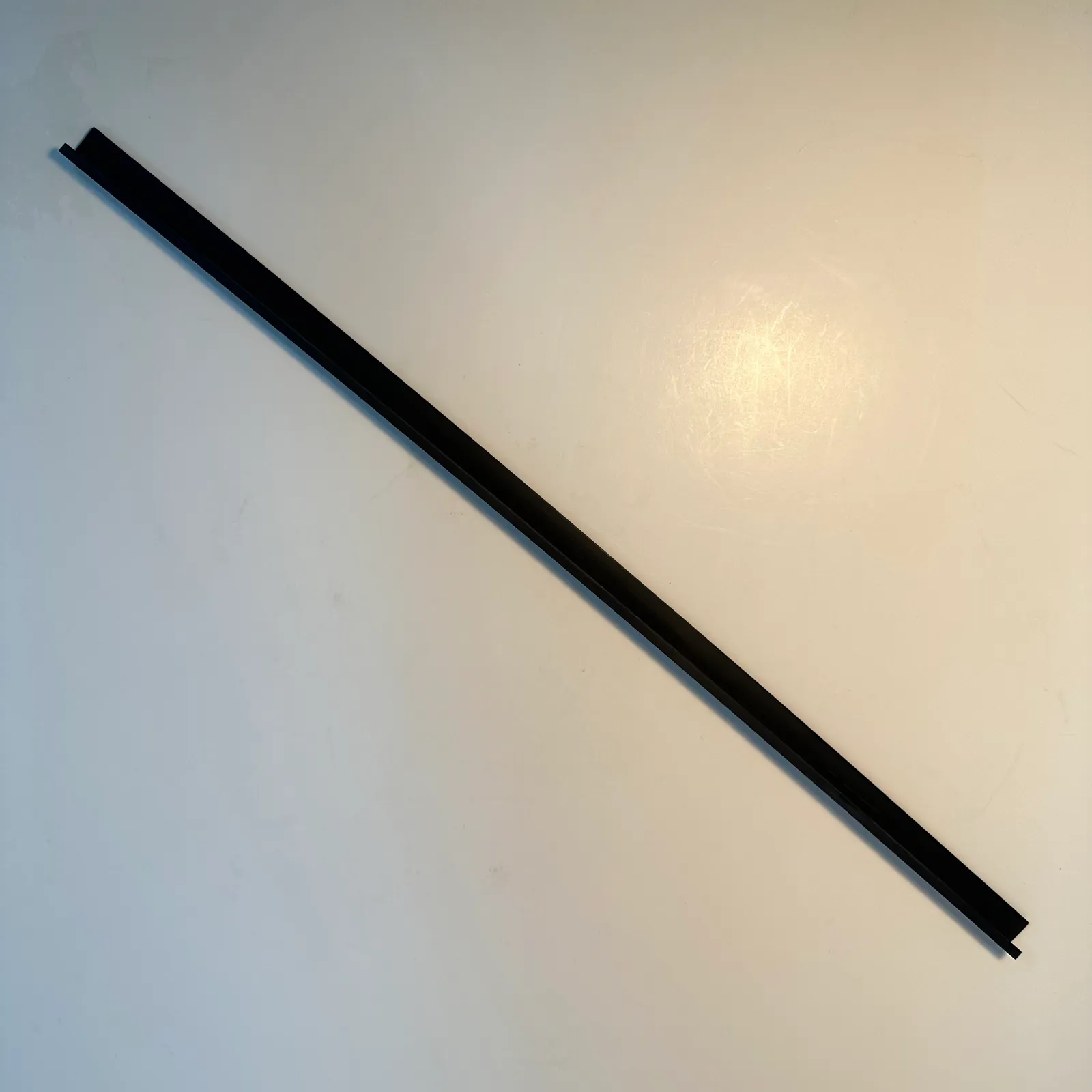 The black angle trim strip seen from above on a white table, running corner to corner