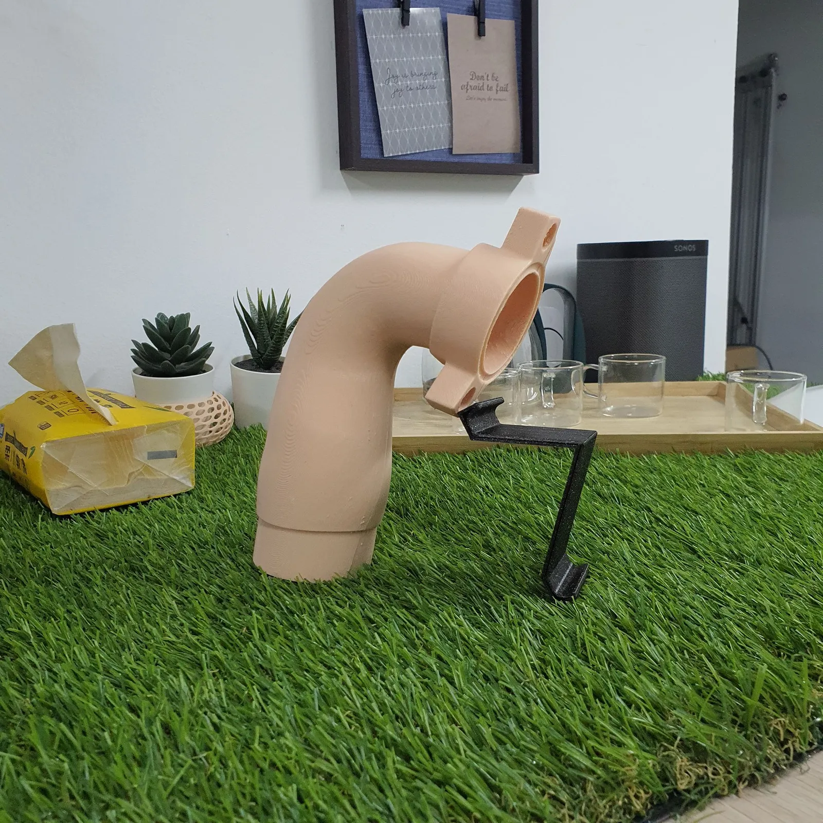 The beige 3D printed pipe elbow standing upright, its flange resting on a bent black 3D printed bracket