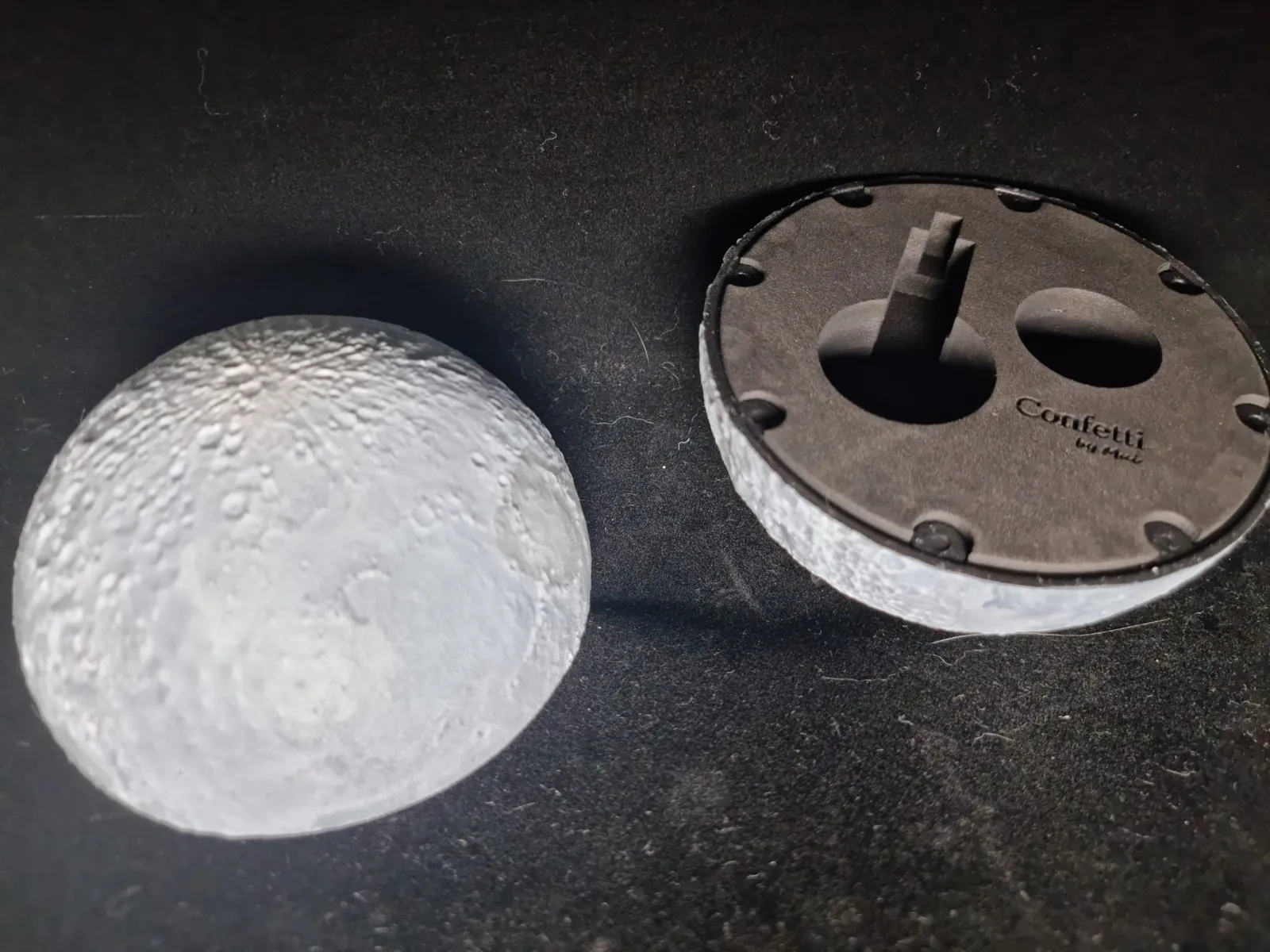 The finished moon jewellery box: one painted half showing its craters beside the other half lying open, with a dark foam insert carrying the Confetti by Mui logo