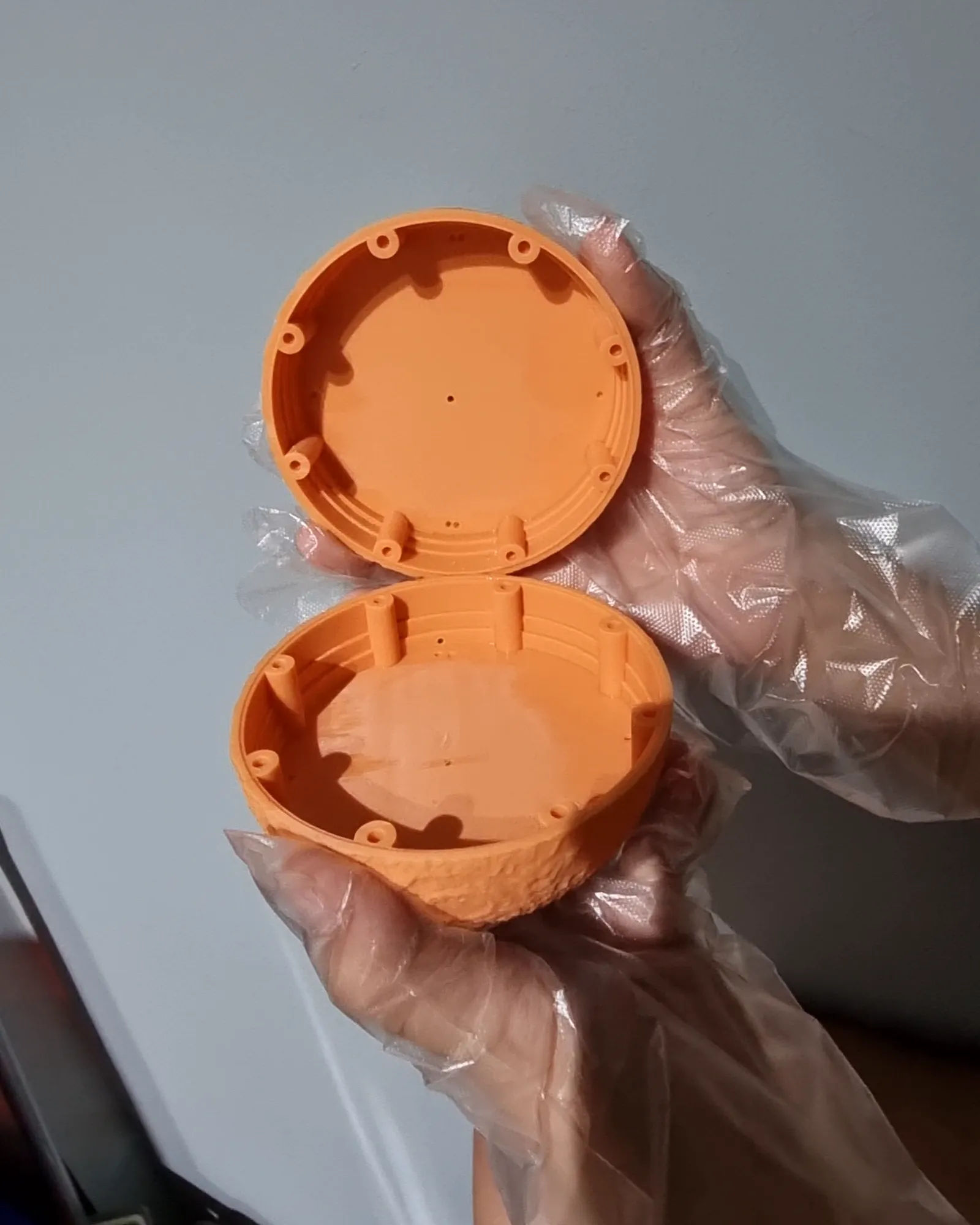 Gloved hands holding the two unpainted orange resin halves open, showing the ring of magnet posts inside each rim