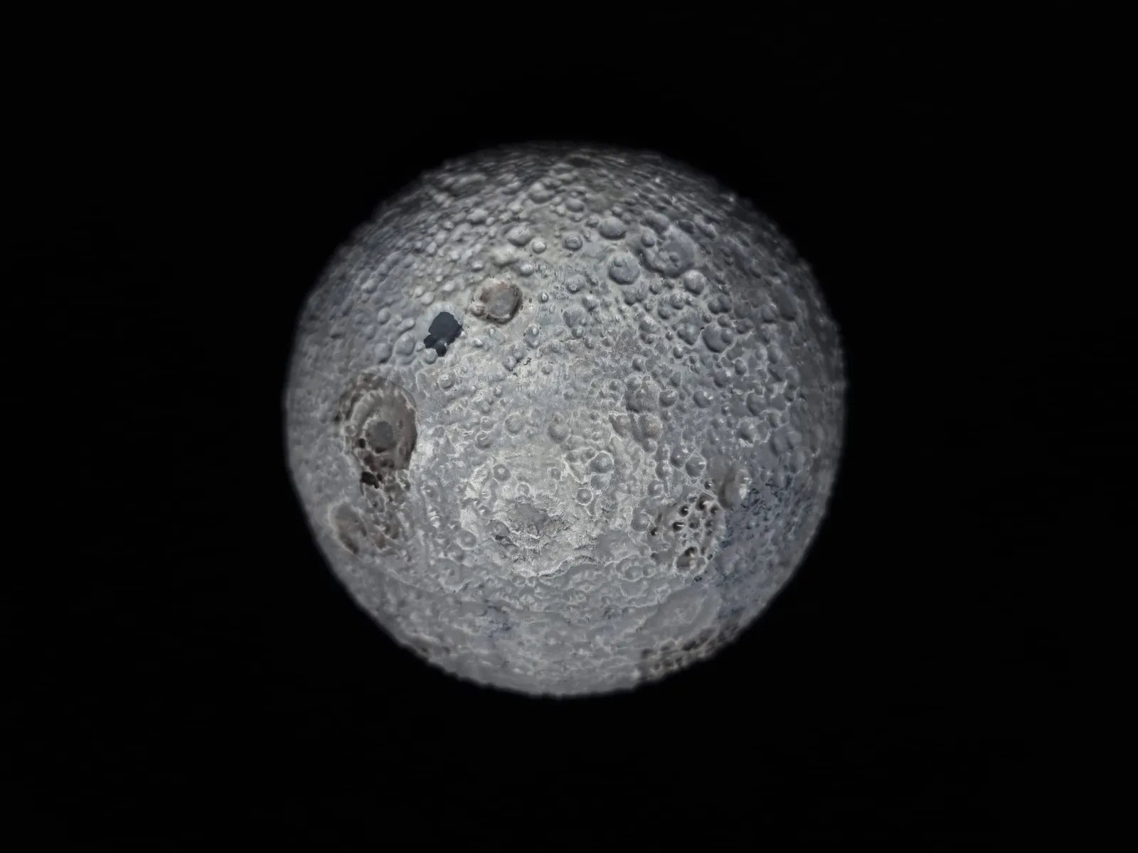 The closed moon box against black, its painted grey surface covered in raised craters