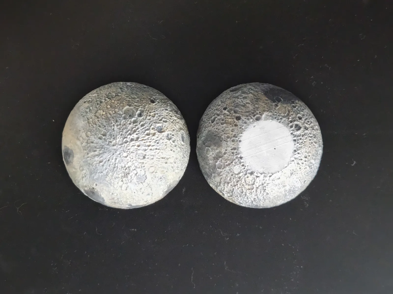 Both painted halves of the moon turned outside up on a dark surface, showing the craters on each