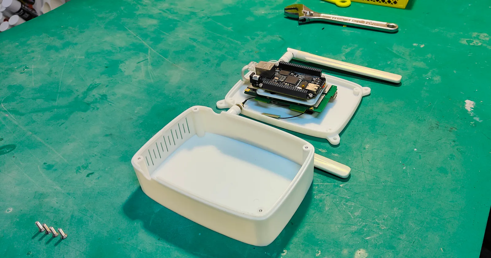 The printed white lid upturned on the workbench, with vent slots in its end, and the base behind it holding the boards and an antenna