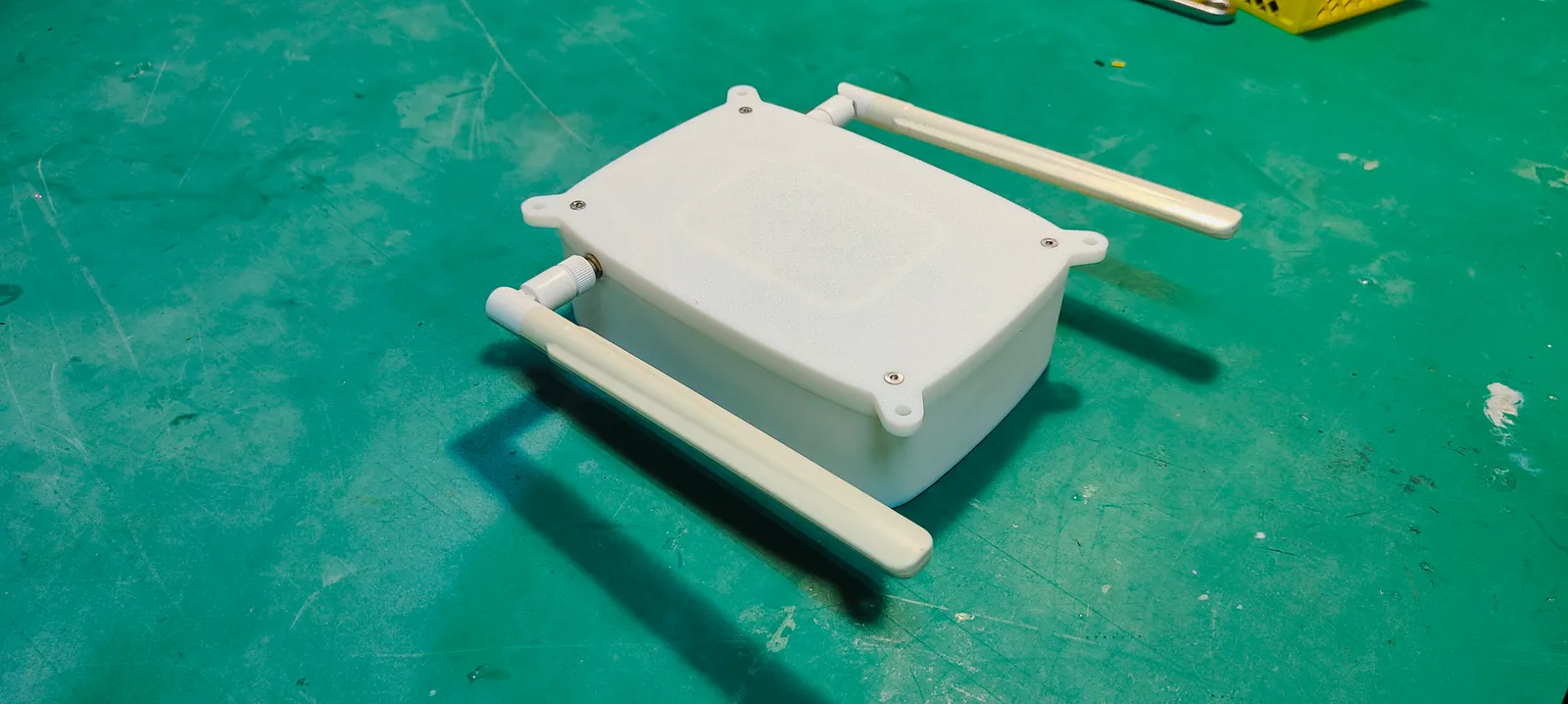 The case from above on the workbench: the lid held by four corner screws, the mounting ears and both antennas laid flat