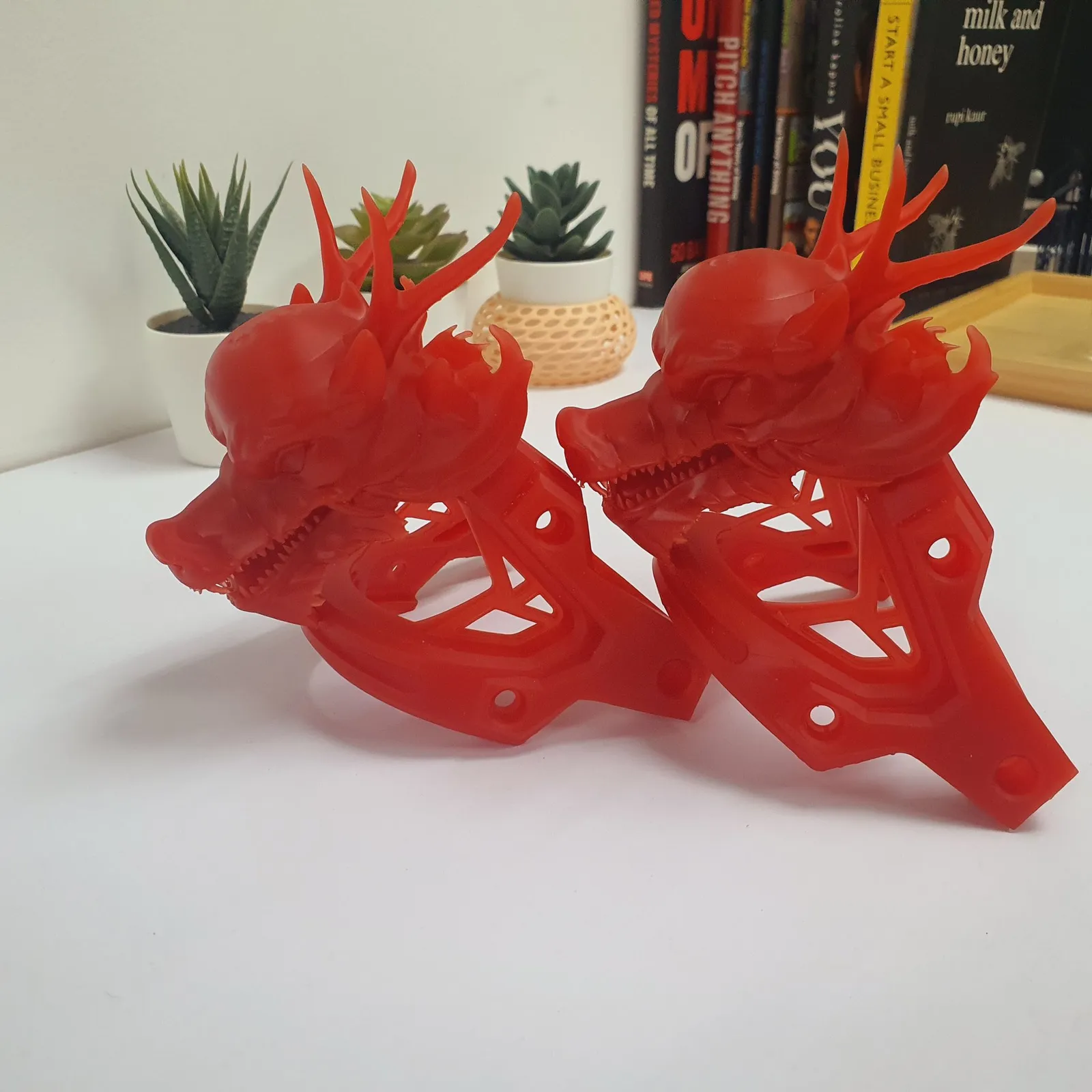 The two dragon heads and brackets printed in translucent red resin, side by side on a white table