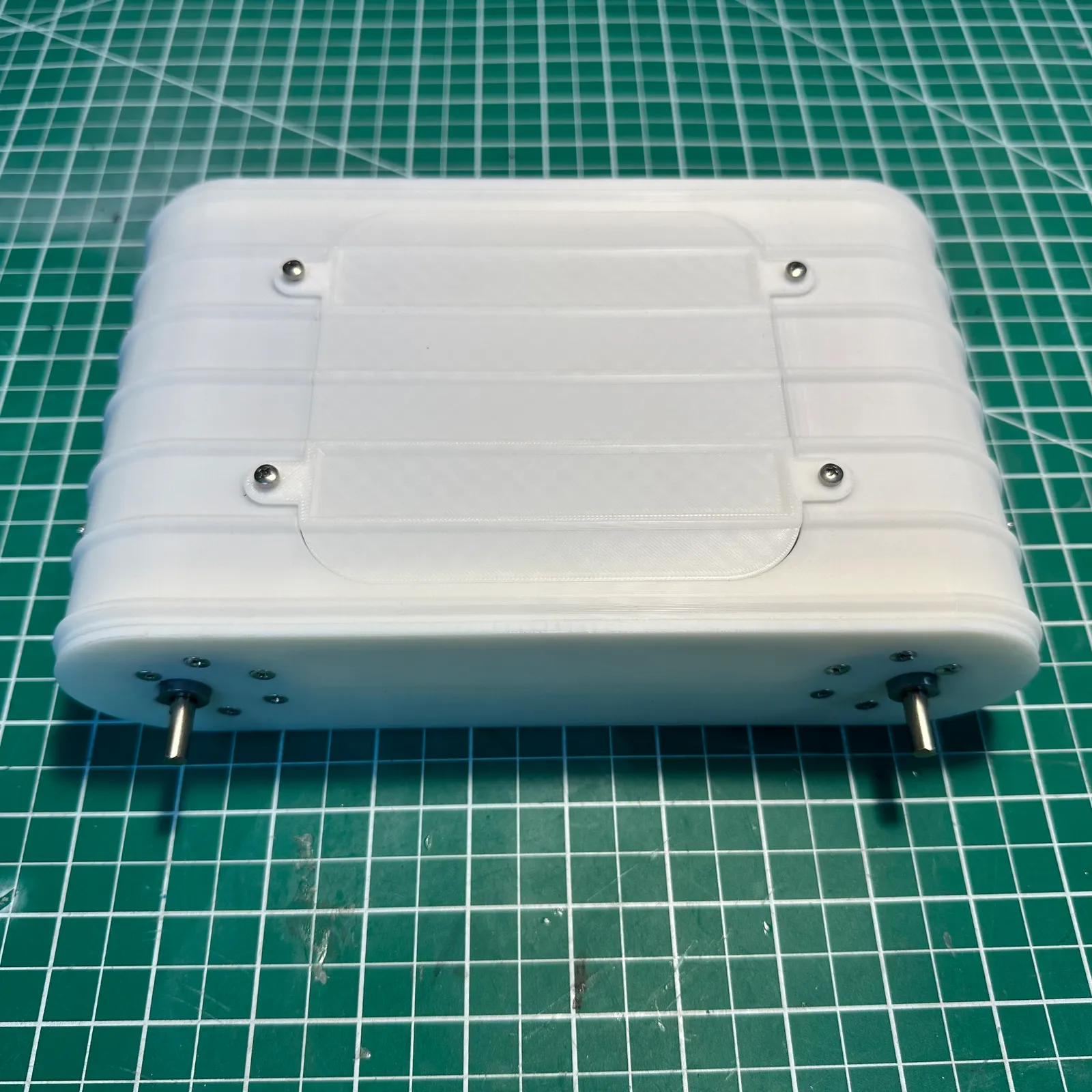 The finished white housing on a green cutting mat: a ribbed shell with a screwed-down lid and a metal motor shaft out of each end