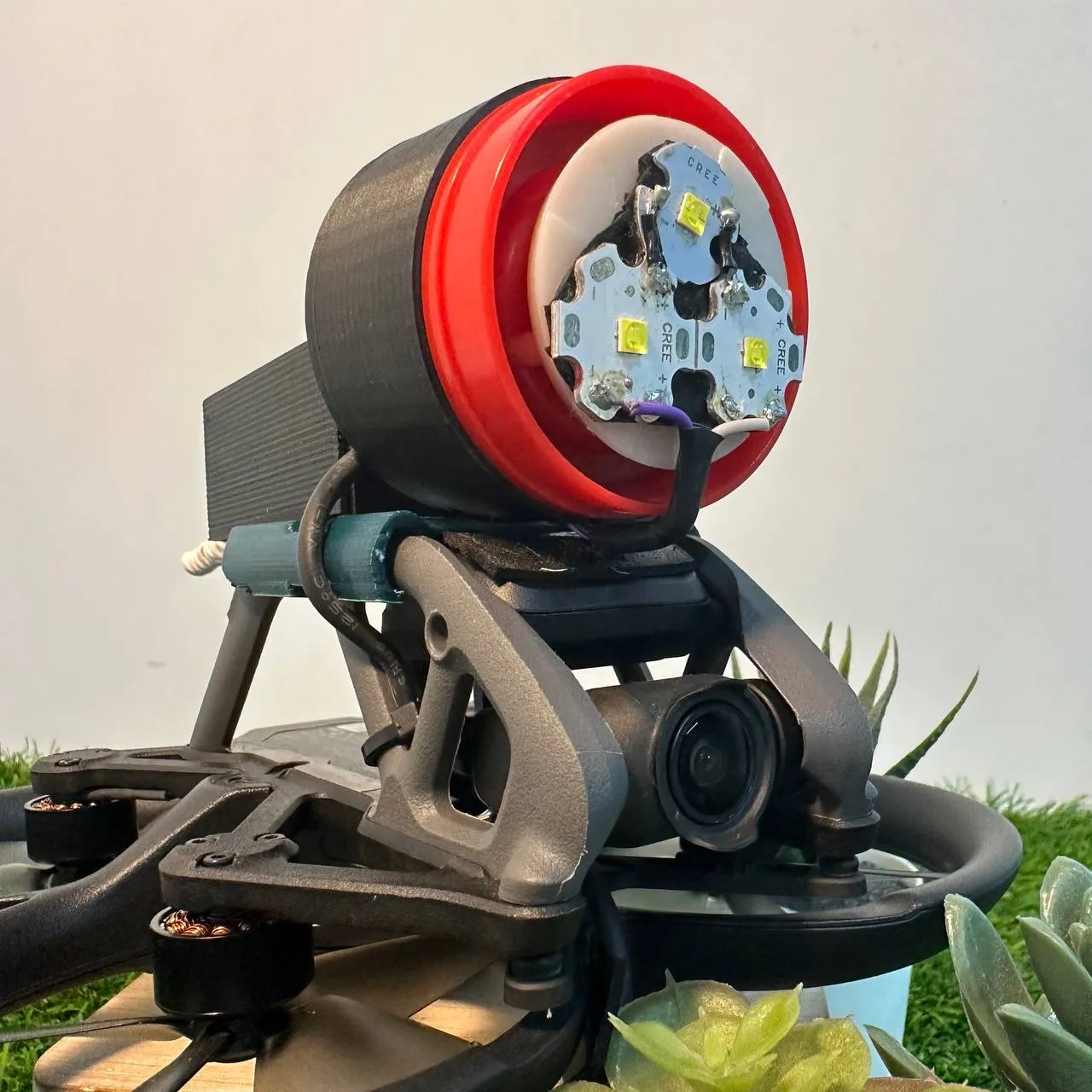 Close view of the spotlight on the drone: three LEDs on a round board inside a red rim and black housing, above the drone's camera