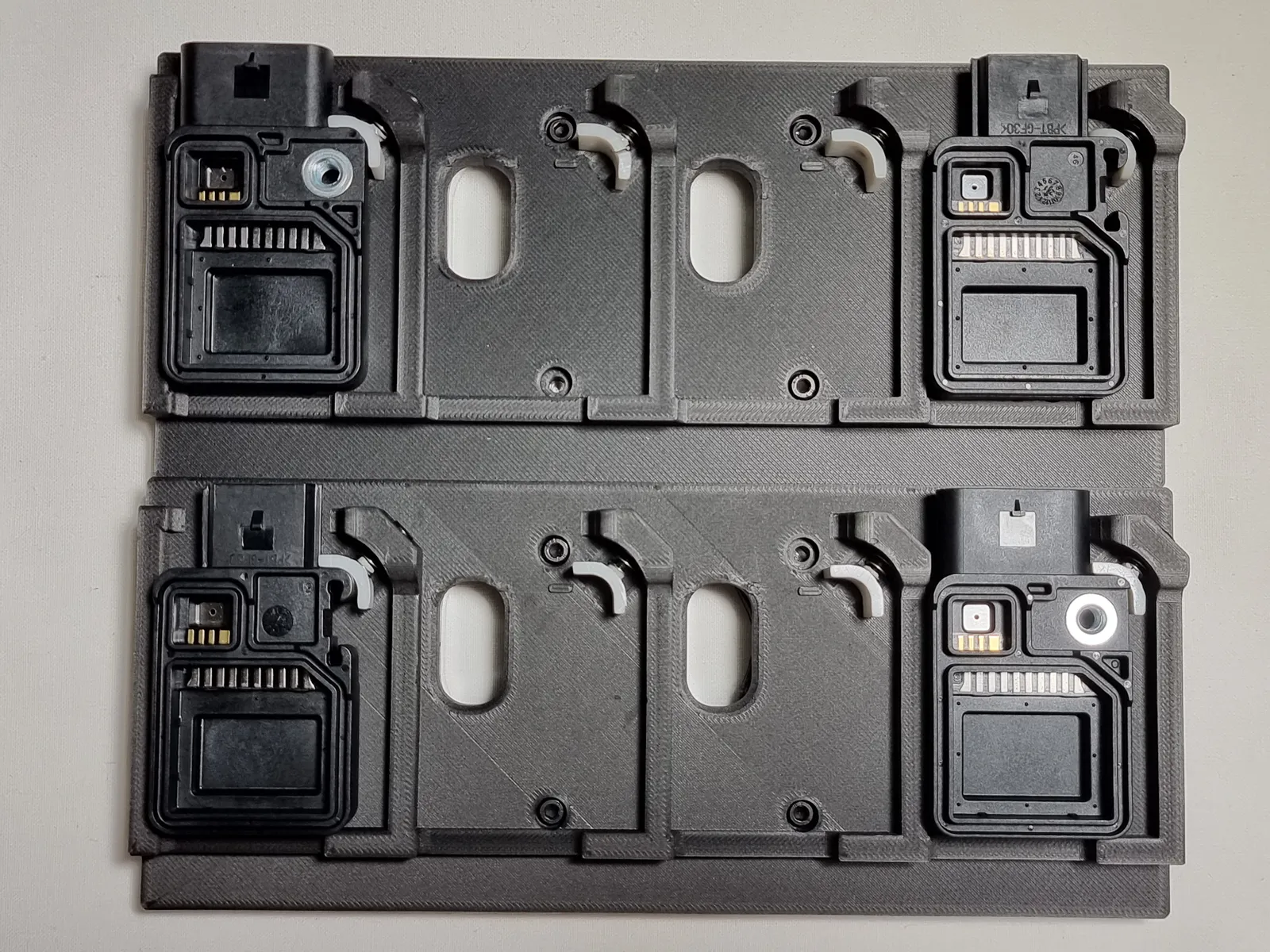 Top view of the plate: two trays of four pockets, with a black electronic part locked in each end pocket and the middle pockets empty