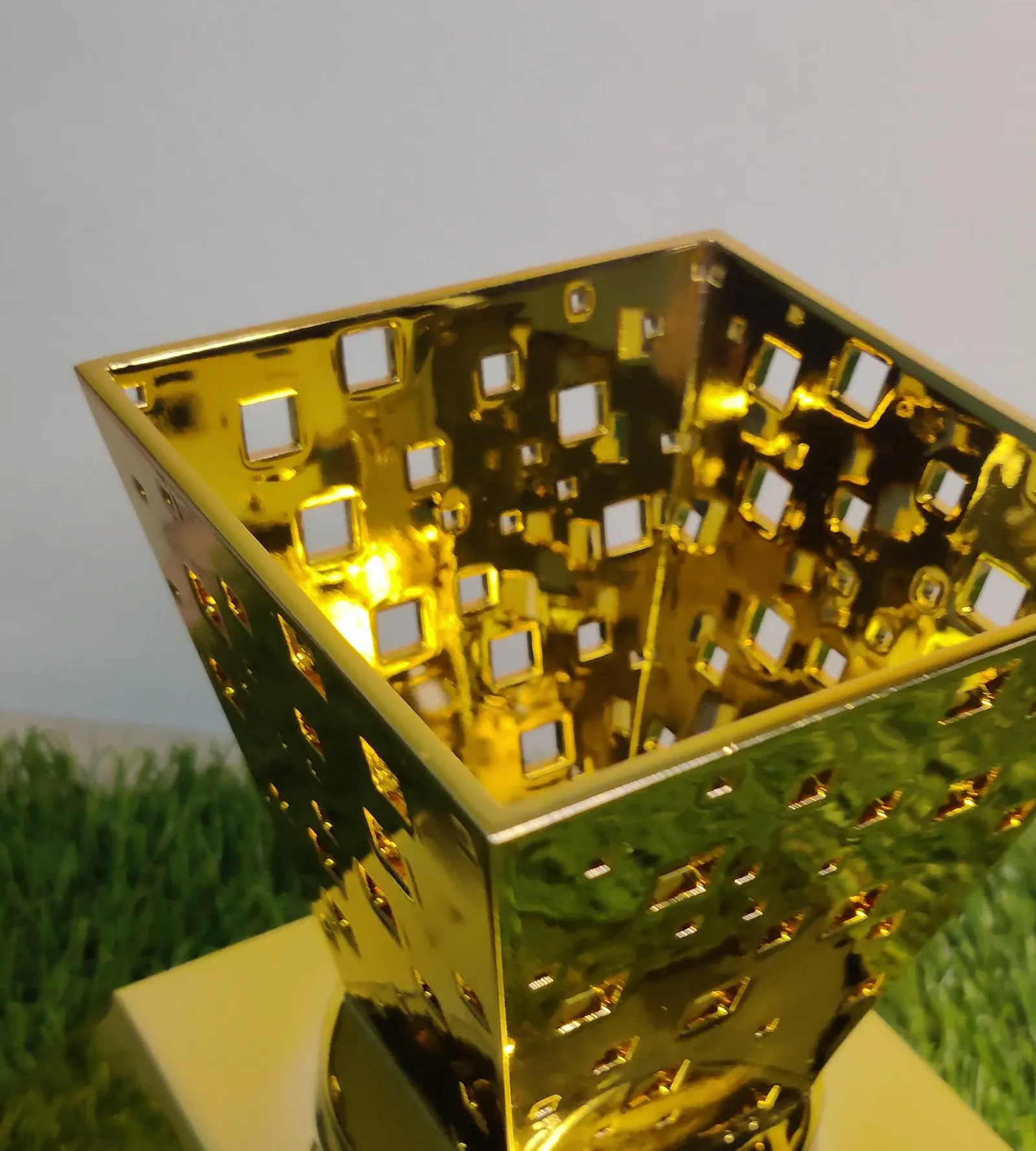 Close-up of the urn's rim from above, with mirror gold faces and square cut-outs showing the wall behind