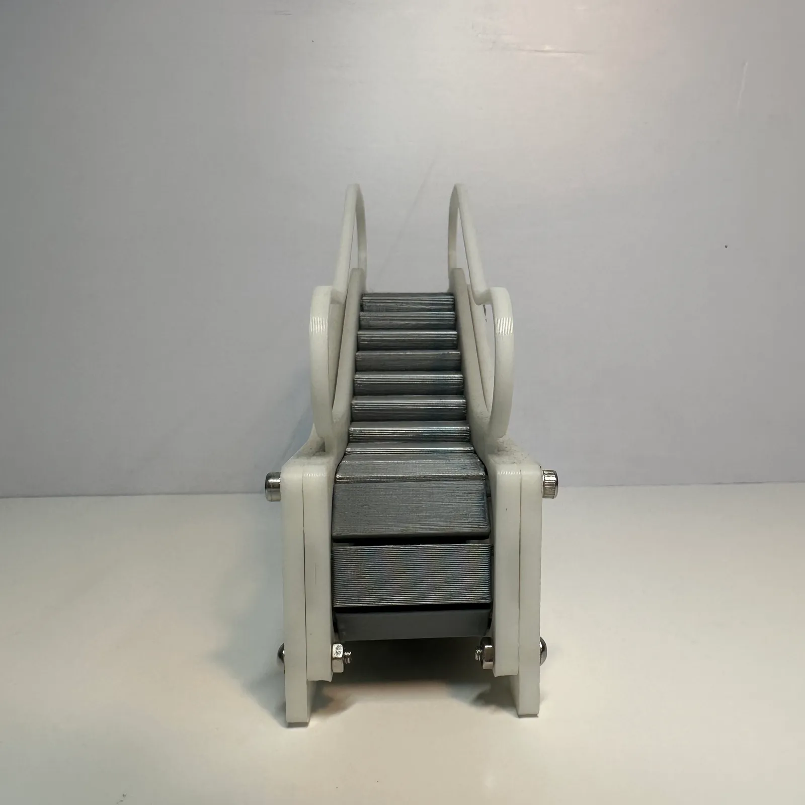 The finished escalator model head-on from the bottom landing: the steps rising between two white side frames, with the handrail loops above