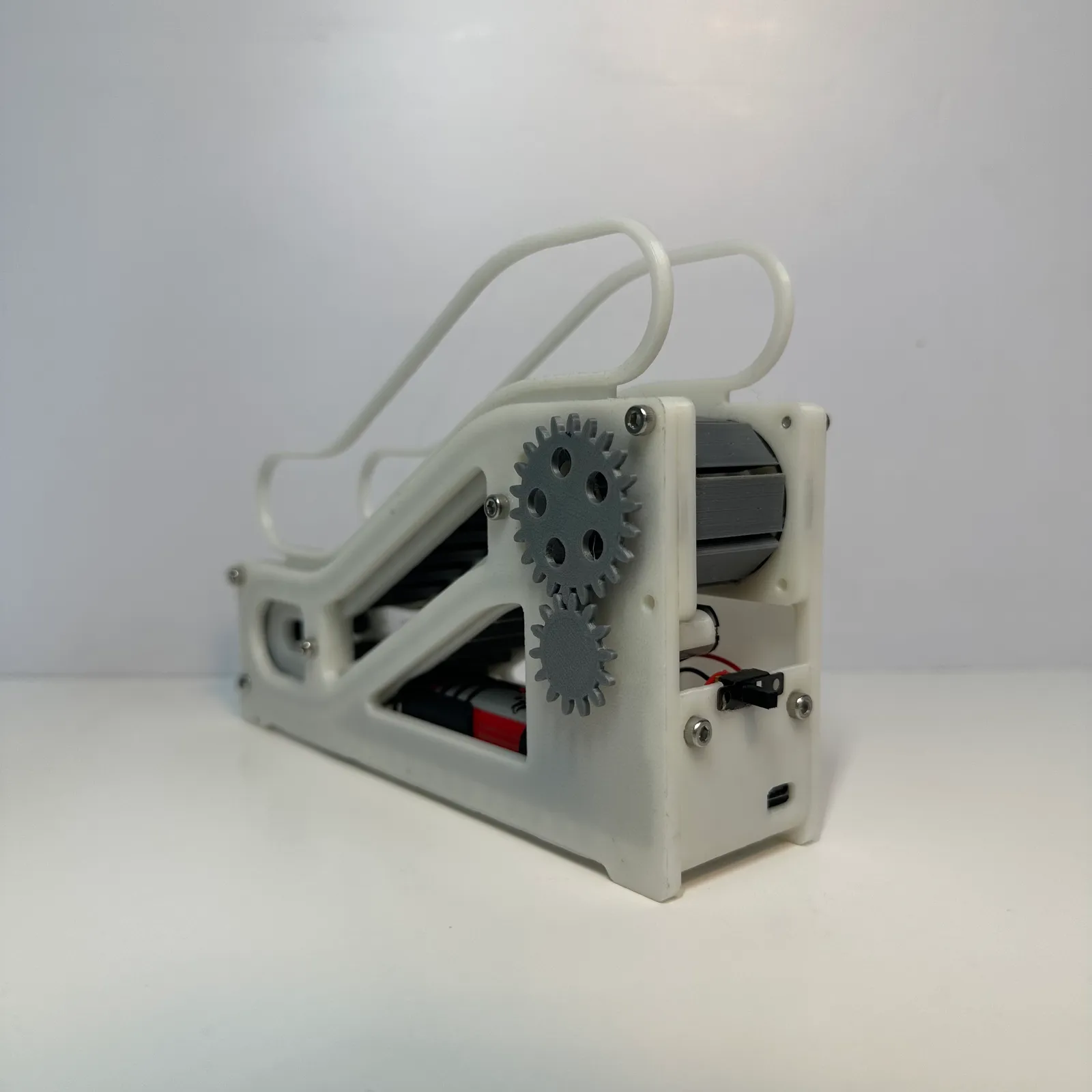 The escalator model from a rear corner: the two grey gears on the side frame, the battery and wiring through the cut-out and the switch at the back